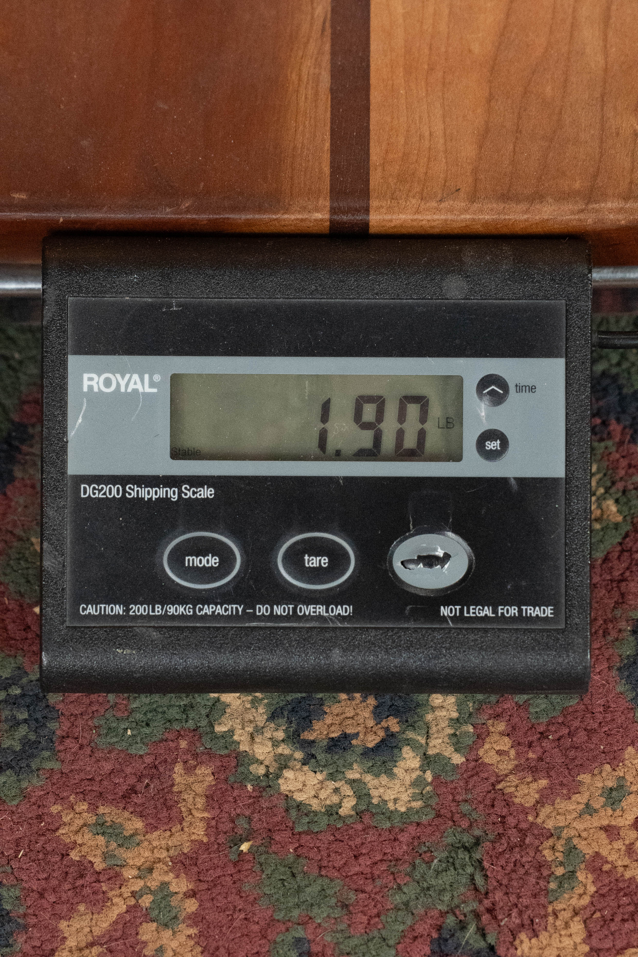 A digital shipping scale on a patterned carpet shows 1.90 pounds. Part of a Weber (Used) 2016 Fern Red Spruce/Flamed Maple A-Style Mandolin #2801 is partially visible above, with several buttons and a caution label on the scale.
