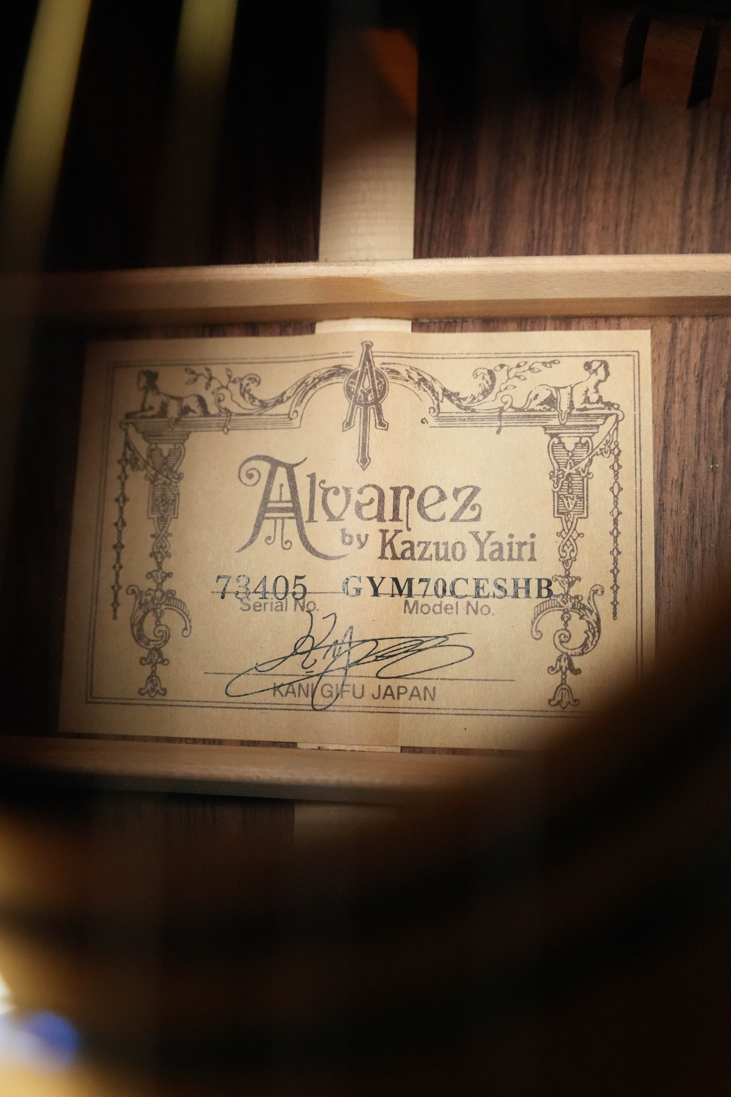 A close-up of the label inside a (Used) 2018 Alvarez Yairi GYM70CESHB Grand Auditorium Acoustic Guitar from The Acoustic Shoppe, showing model #3405, signatures, "Alvarez by Kazuo Yairi," and Kani Gifu Japan, framed by wood beams.