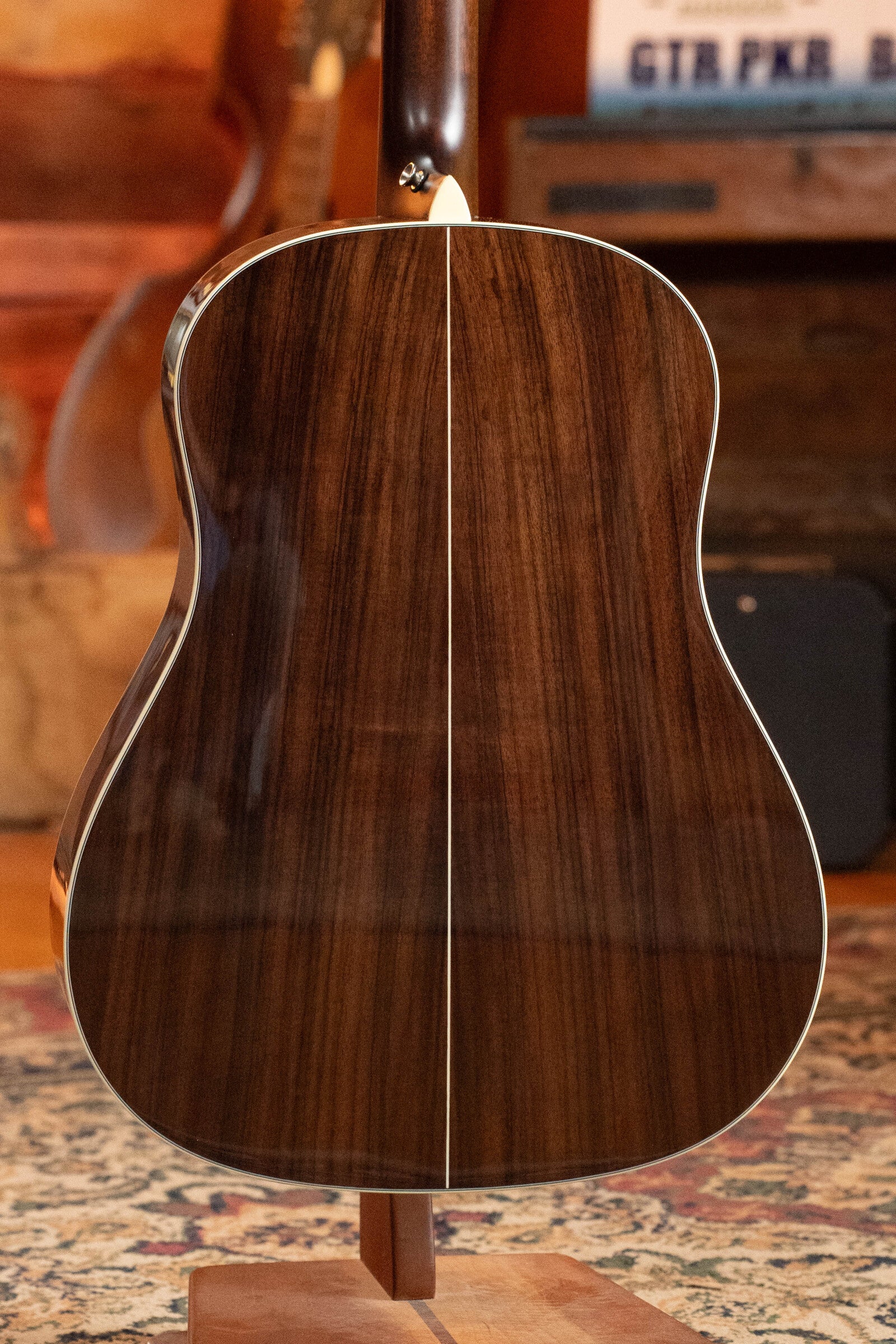 The image shows the back of a Used 2021 Eastman Guitars E20SS Adirondack/Rosewood Slope Shoulder Dreadnought Acoustic Guitar #6671, featuring a glossy dark wood finish with a light center stripe, on a wooden stand in a warmly lit room.