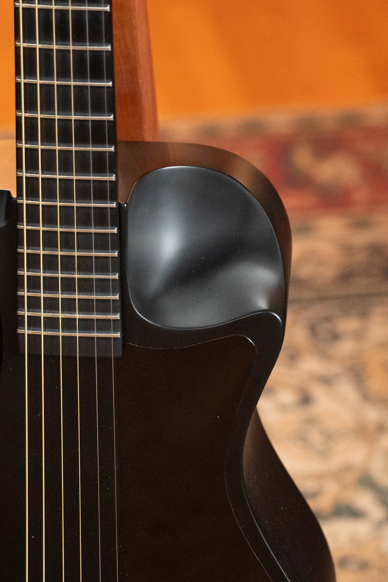 Close-up of a used 2022 Journey Instruments OF660M all carbon fiber compact travel guitar (#5005) with strings, featuring the JouorneyTek-3 pickup. The body and neck are visible against a blurred rug and warm wooden floor background.