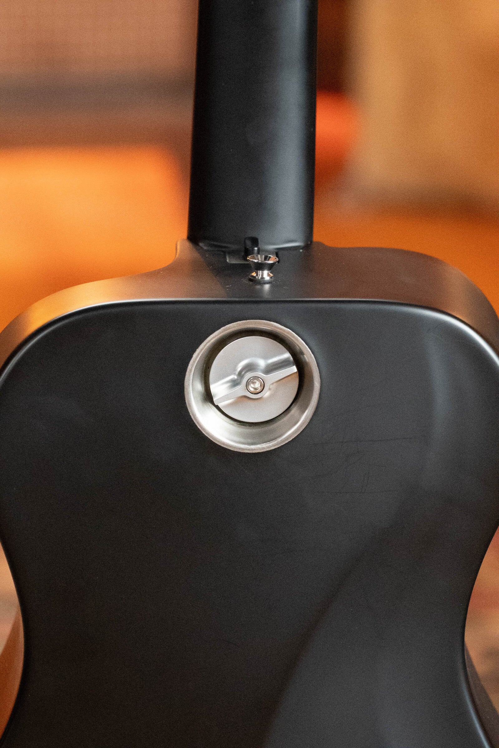 Close-up of the back of a (Used) 2022 Journey Instruments OF660M All Carbon Fiber Compact OO Travel Guitar w/JourneyTek-3 Pickup #5005 shows a circular metal battery compartment with latch near the neck joint.