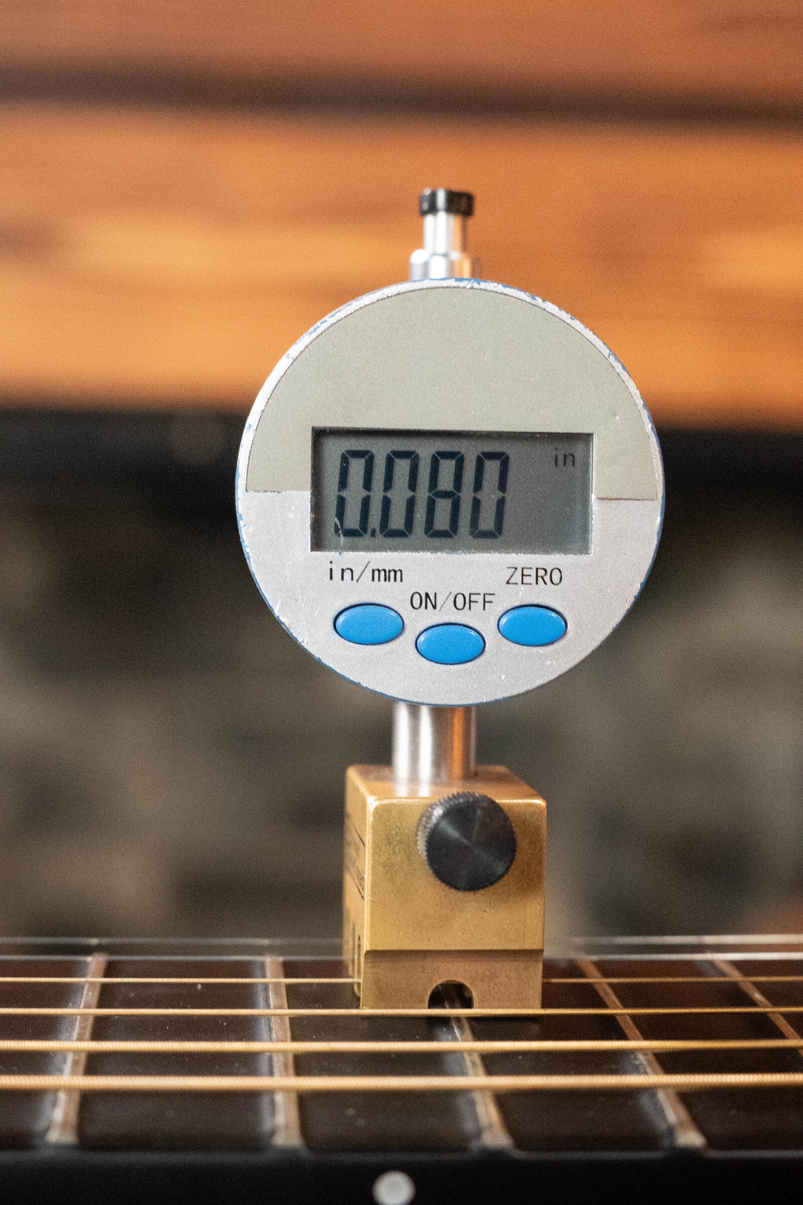 A digital gauge reads 0.080 inches atop the fretboard of a (Used) 2022 Journey Instruments OF660M All Carbon Fiber Compact OO Travel Guitar w/JourneyTek-3 Pickup #5005, with metal strings visible and a blurred background.