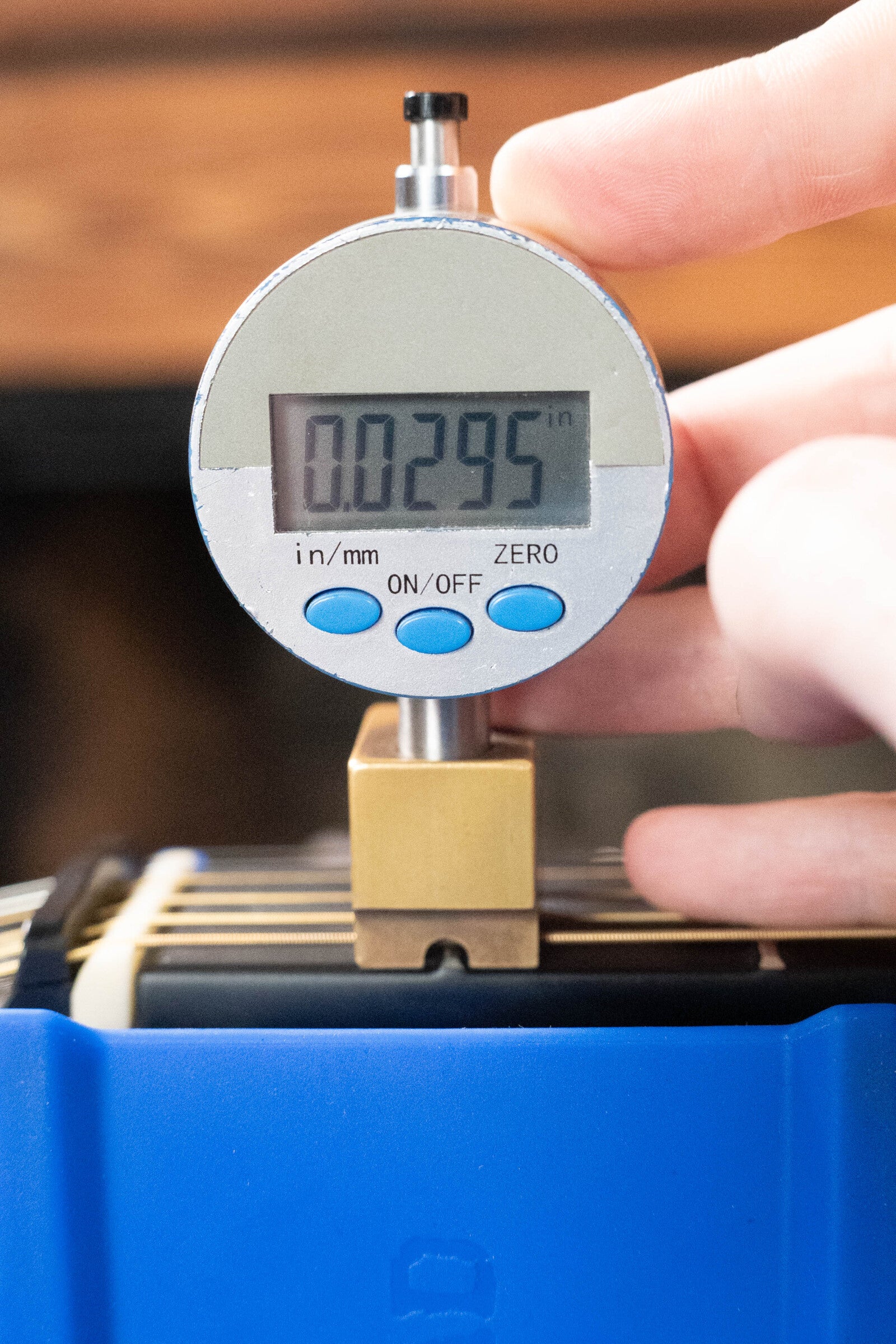 A close-up of a digital dial indicator (0.0295 in) being adjusted, positioned on stacked materials in a blue holder, beside a Journey Instruments (Used) 2022 OF660M All Carbon Fiber Compact Travel Guitar w/JourneyTek-3 Pickup #5005.
