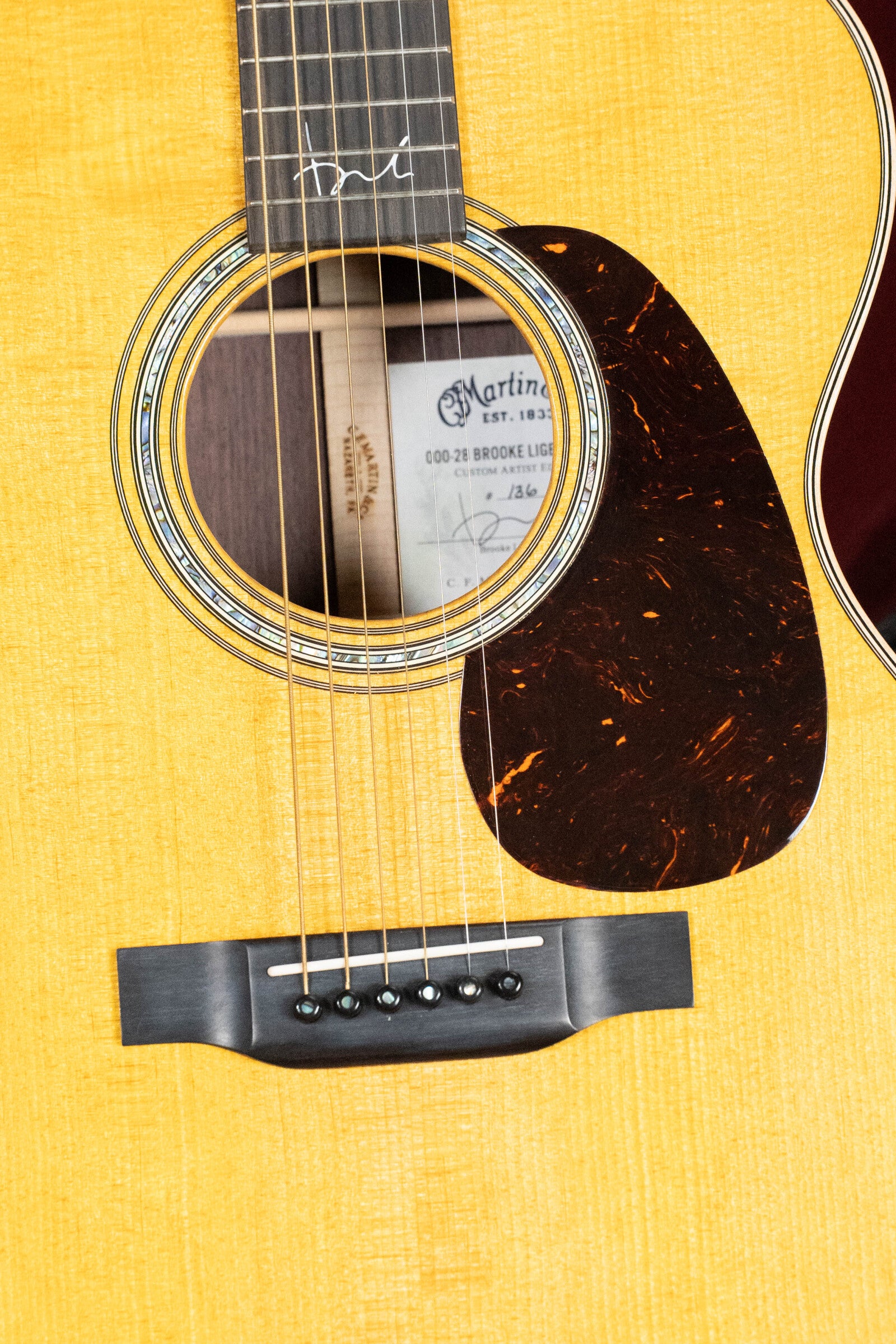 Close-up of a 2022 Martin & Co. Brook Ligertwood 000-28 Spruce/Rosewood OOO acoustic guitar’s body, highlighting the sound hole, strings, pickguard, bridge, and interior label with the model name.