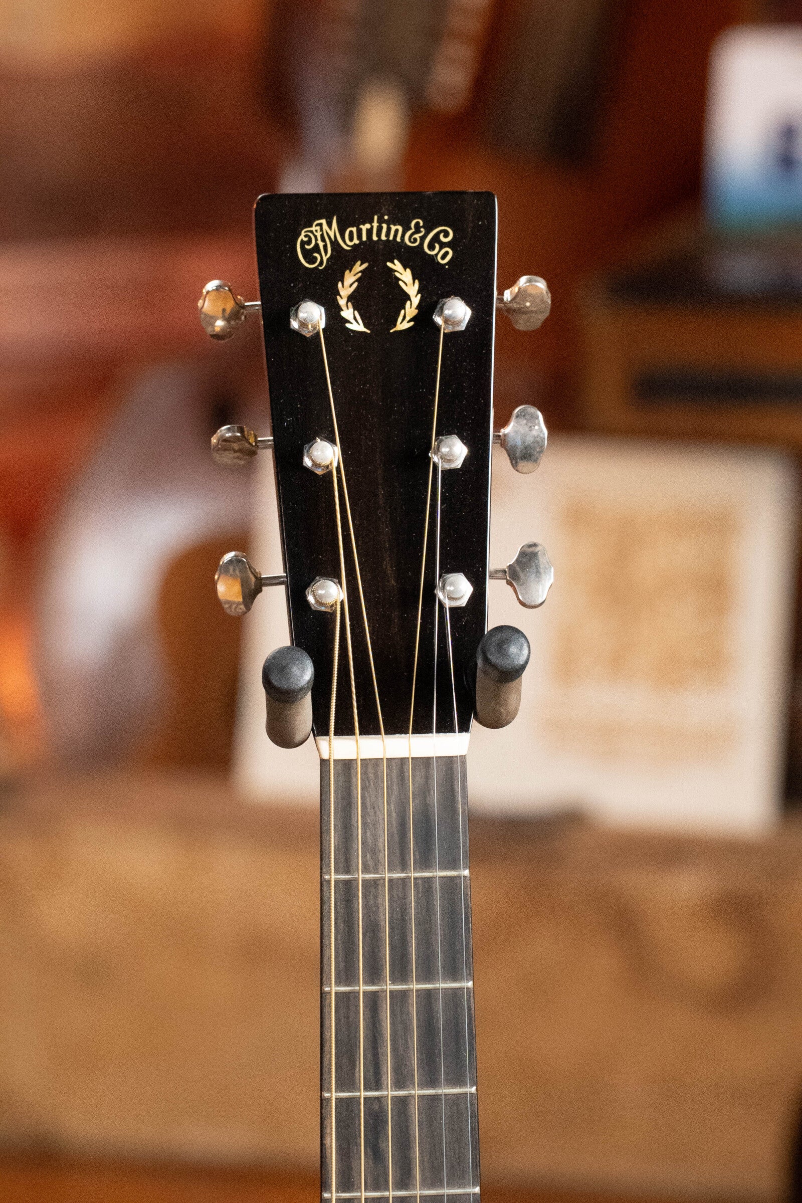 Close-up of the headstock of a (Used) 2022 Martin Brook Ligertwood 000-28 Spruce/Rosewood OOO Acoustic Guitar by Martin & Co., showing tuning pegs and logo against a blurred background.