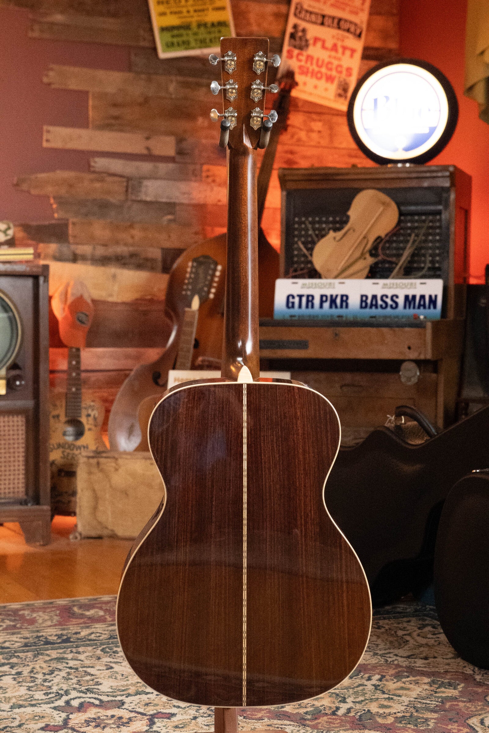 A (Used) 2022 Martin Brook Ligertwood 000-28 Spruce/Rosewood OOO Acoustic Guitar by Martin & Co. stands upright in a cozy, vintage-style room filled with music gear, old posters, and stringed instruments.