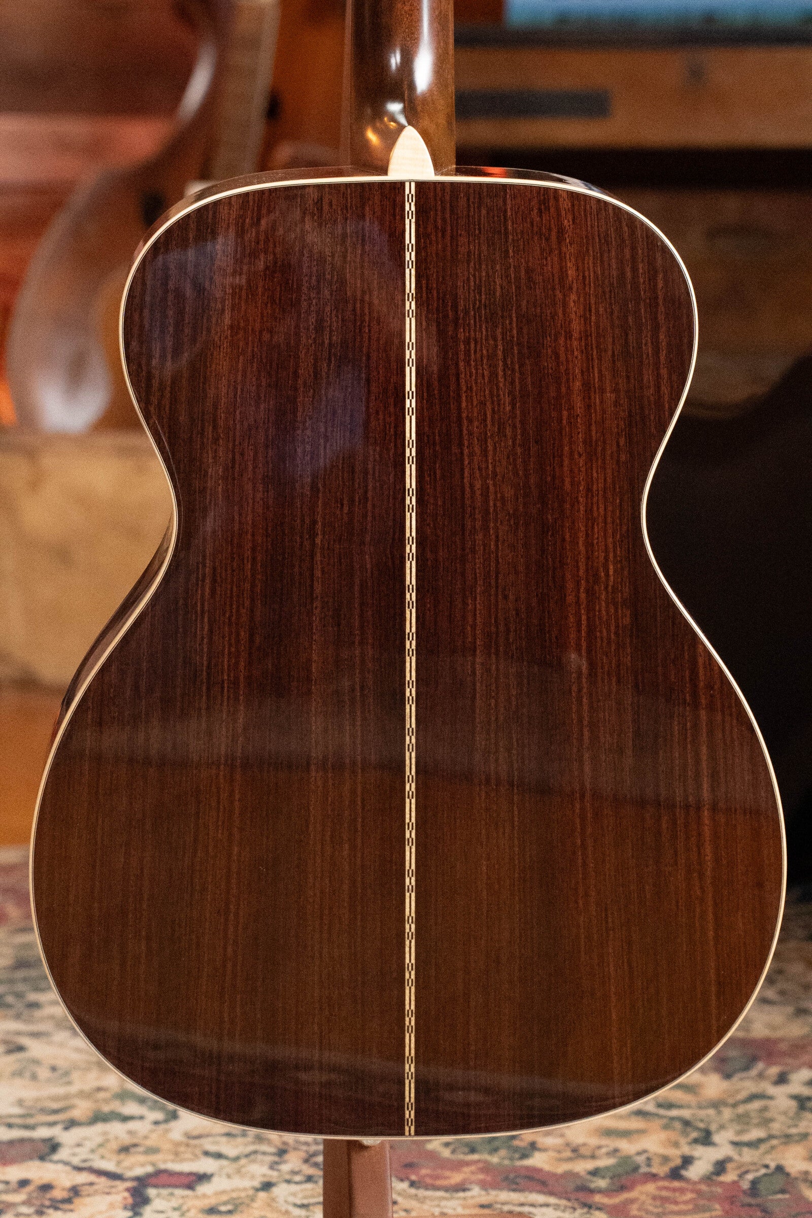 The image shows the back of a (Used) 2022 Martin Brook Ligertwood 000-28 Spruce/Rosewood OOO Acoustic Guitar by Martin & Co., featuring dark polished East Indian rosewood with a light-colored center strip, upright on a patterned rug.