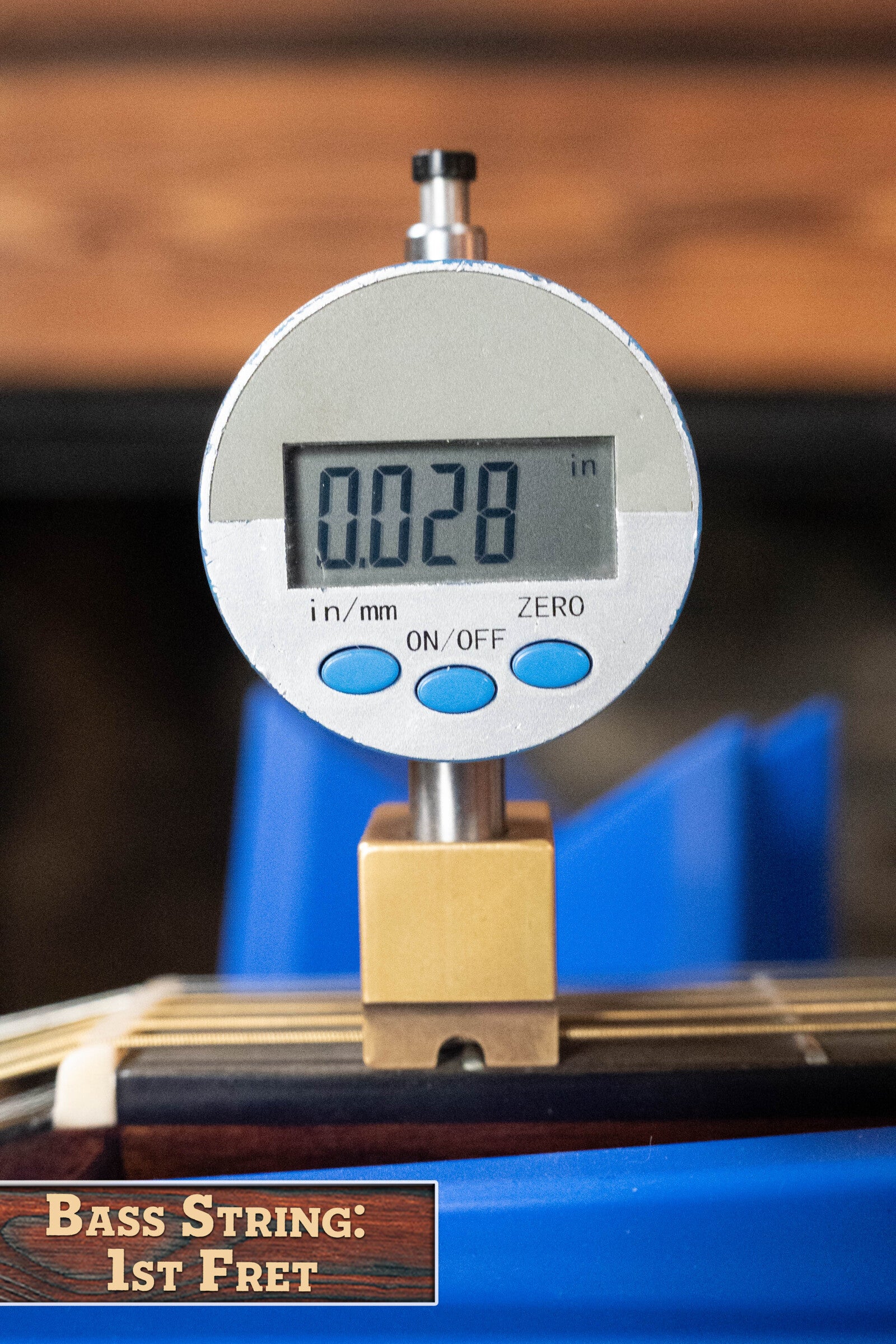 A digital gauge shows 0.028 inches above the first fret of a bass string on a Martin & Co. (Used) 2022 Brook Ligertwood 000-28 Spruce/Rosewood OOO Acoustic Guitar. At the bottom: “Bass String: 1st Fret.”.