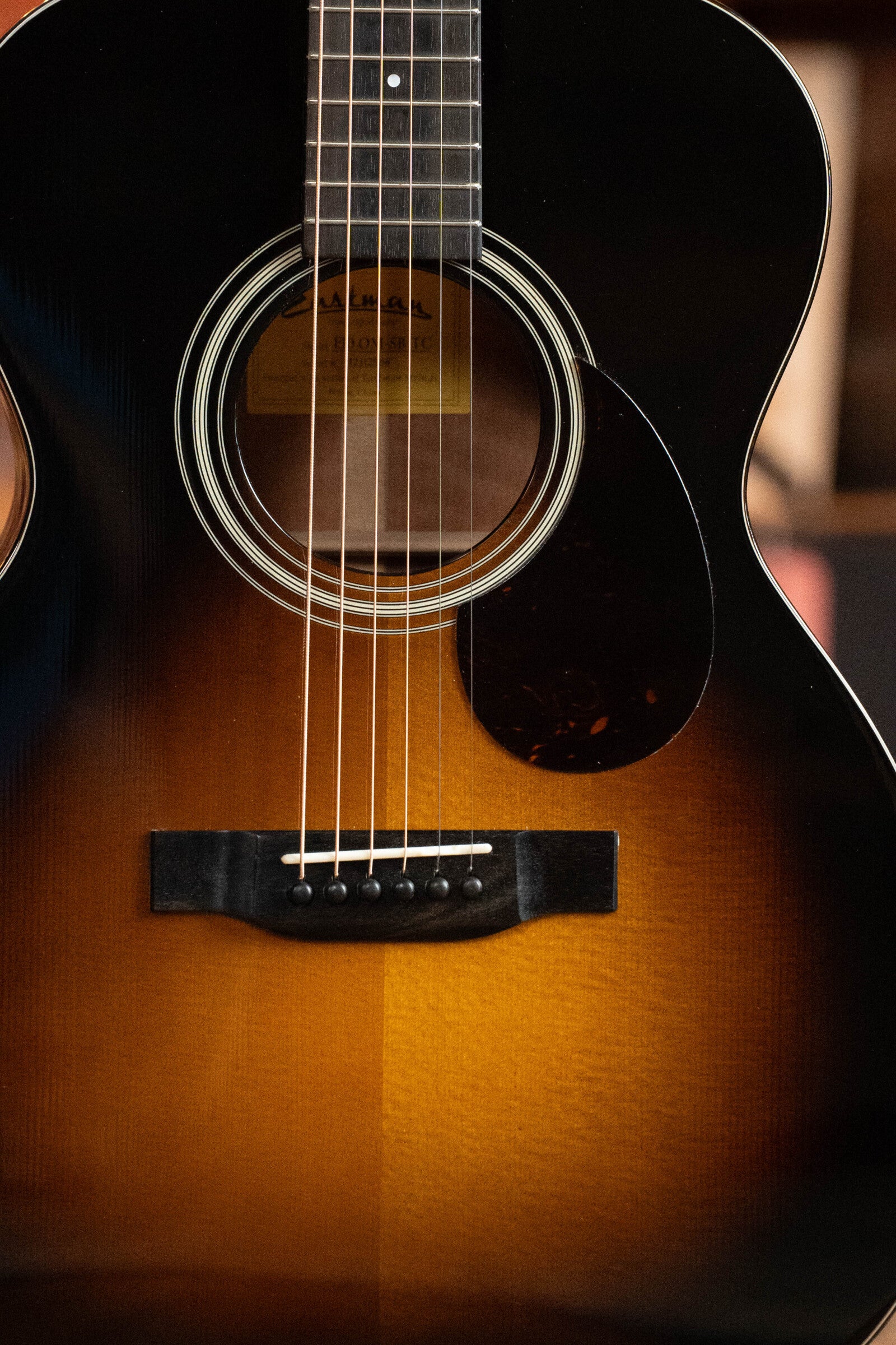 Close-up of a (Used) 2023 Eastman E10OM-TC-SB Orchestra acoustic guitar by Eastman Guitars, featuring a Thermo-Cured Adirondack spruce top, mahogany back and sides, sunburst finish, and detailed wood grain near the bridge and pickguard.