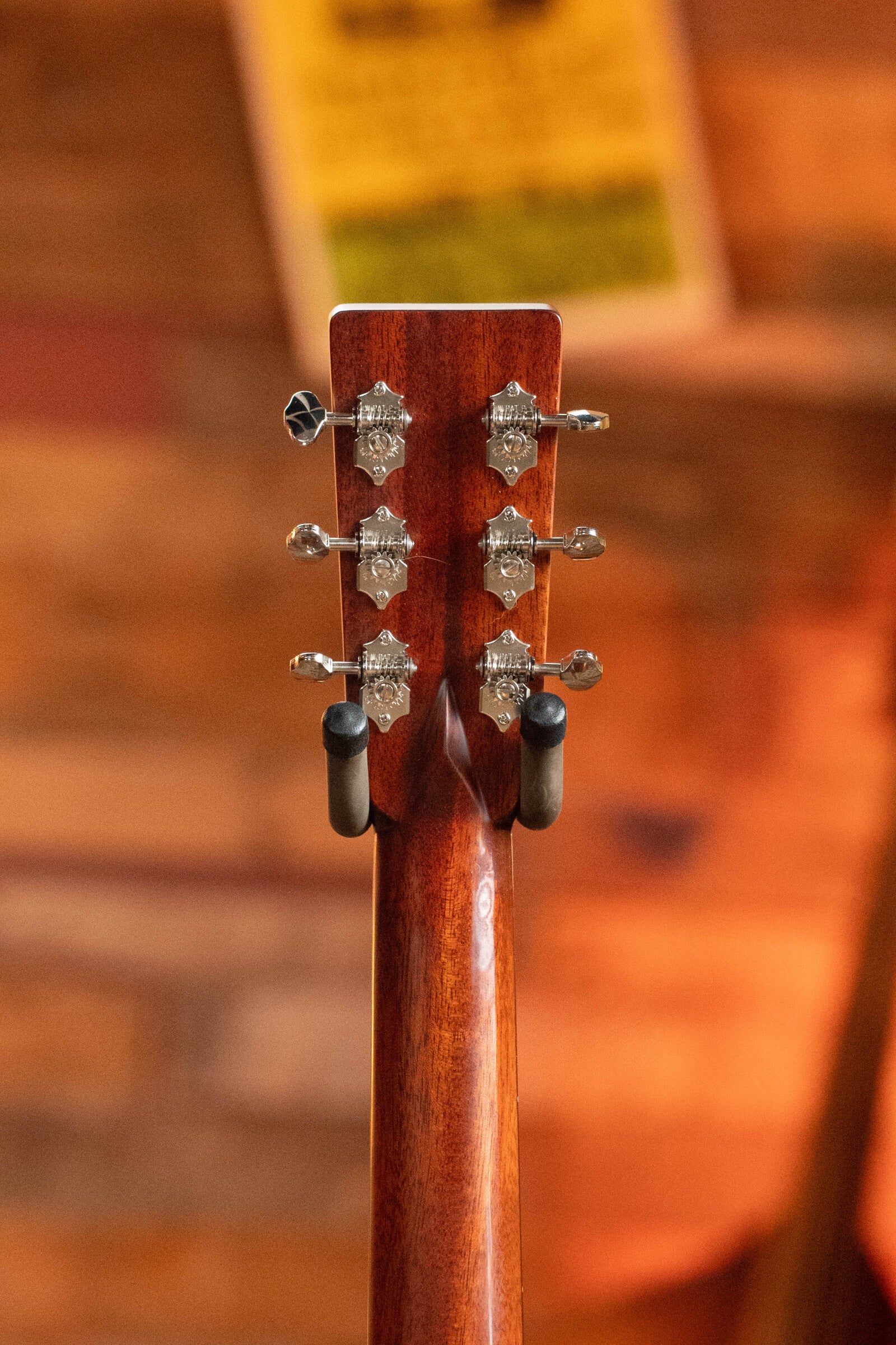 Close-up of the back of a (Used) 2023 Eastman Guitars E10OM-TC-SB Orchestra Model Acoustic Guitar #2966, showing six metal tuners on the headstock and a wooden neck, set against a blurred wooden background.