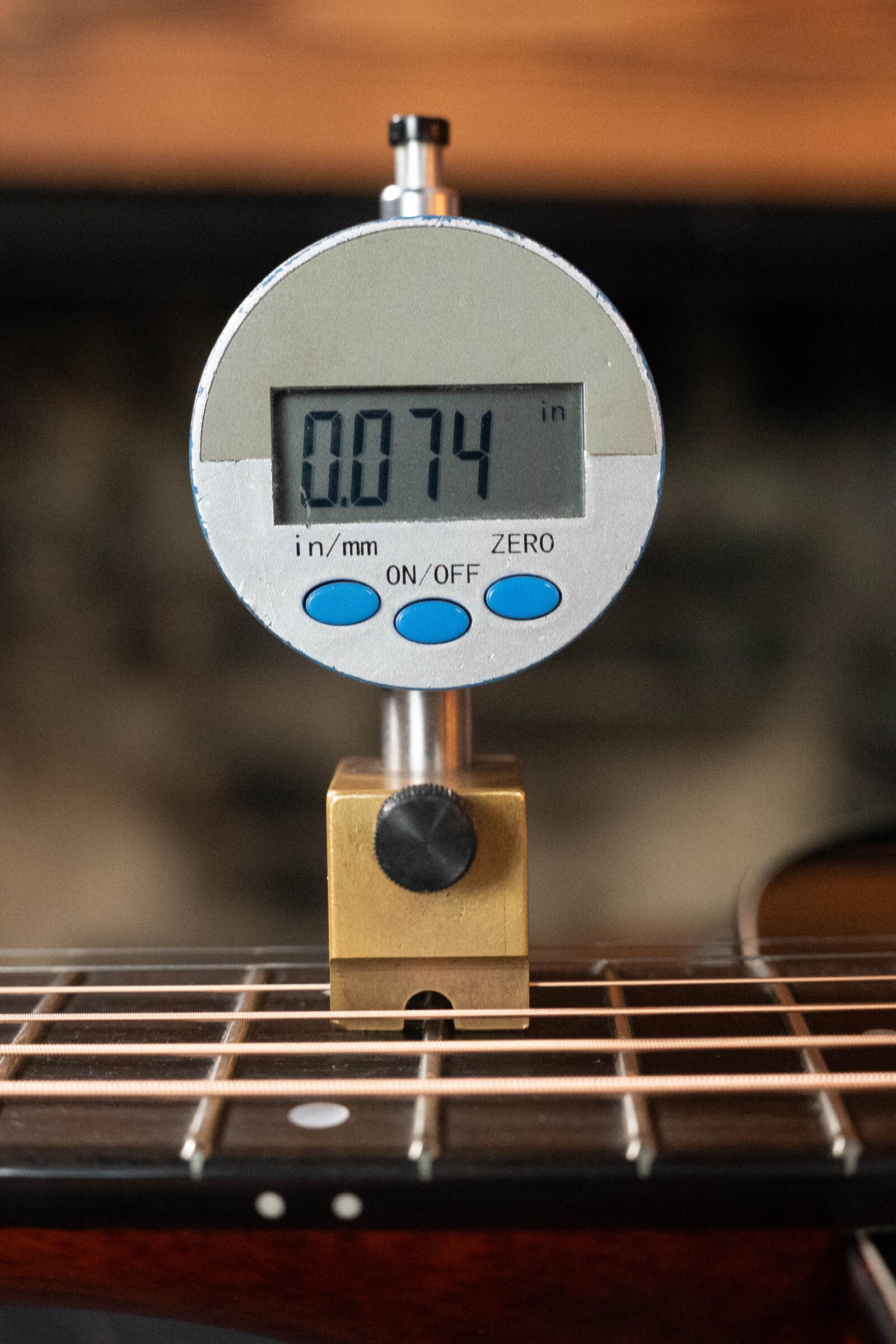 A digital gauge reads 0.074 inches, positioned vertically on an Eastman Guitars (Used) 2023 E10OM-TC-SB Thermo-Cured Adirondack/Mahogany Sunburst Orchestra Model Acoustic Guitar #2966 to check the string height above the fretboard.