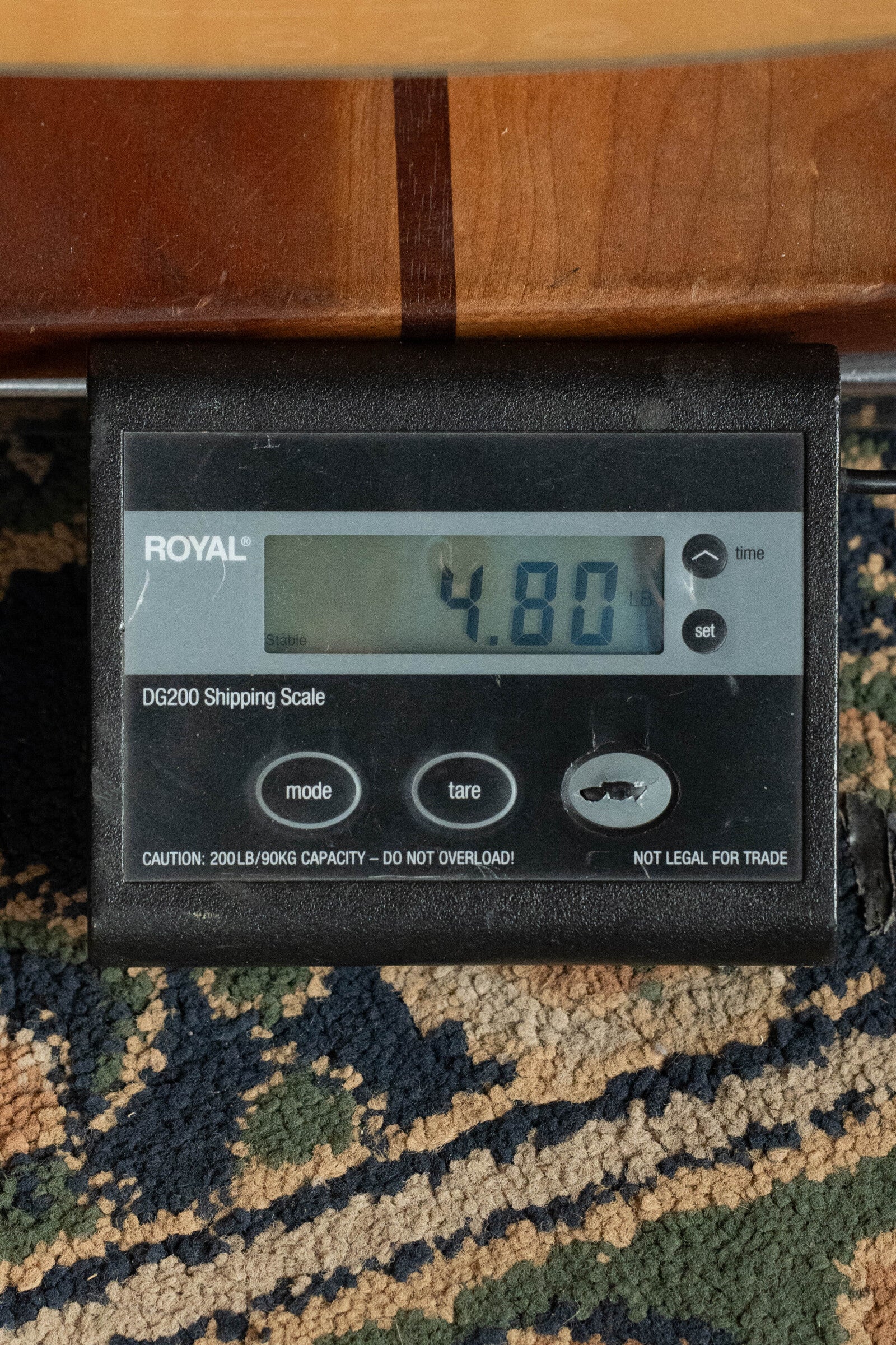 A digital shipping scale labeled ROYAL DG200 shows 4.80 pounds. Next to it on a patterned carpet is a used 2024 Alvarez AD60 Sitka/Mahogany Dreadnought Acoustic Guitar #0300 by Alvarez from the Artist Series.
