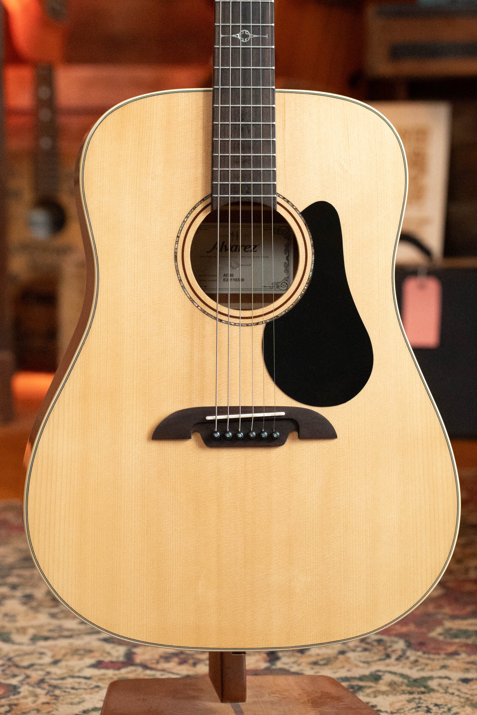 A (Used) 2024 Alvarez AD60 Sitka/Mahogany Dreadnought Acoustic Guitar #0300 is shown upright indoors on a patterned rug, featuring a natural wood finish, black pickguard, and dark bridge. Brand: Alvarez.