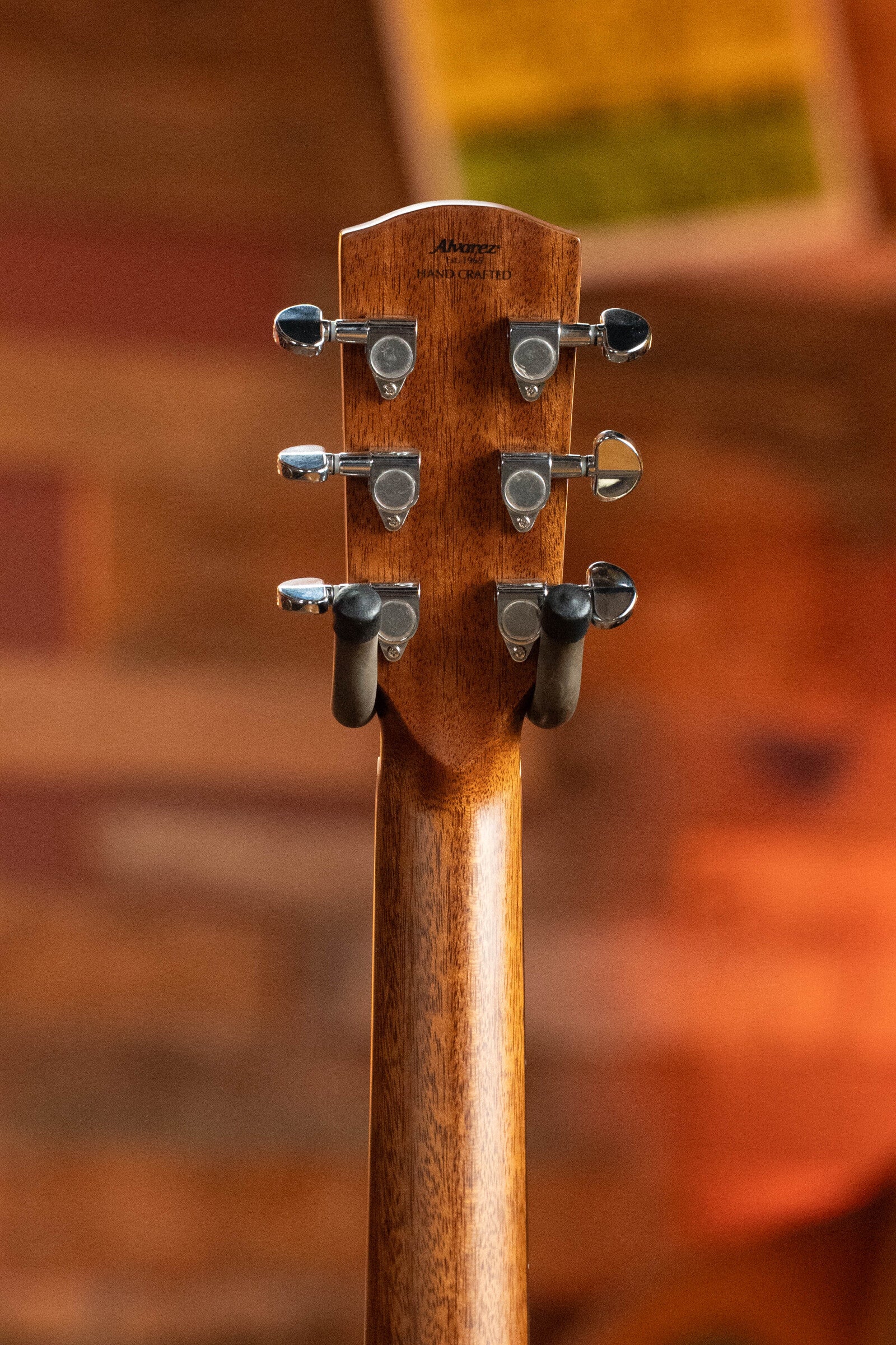 Close-up of the back headstock and tuning pegs on this (Used) 2024 Alvarez AD60 Sitka/Mahogany Dreadnought Acoustic Guitar #0300, with a blurred wooden background and warm lighting.