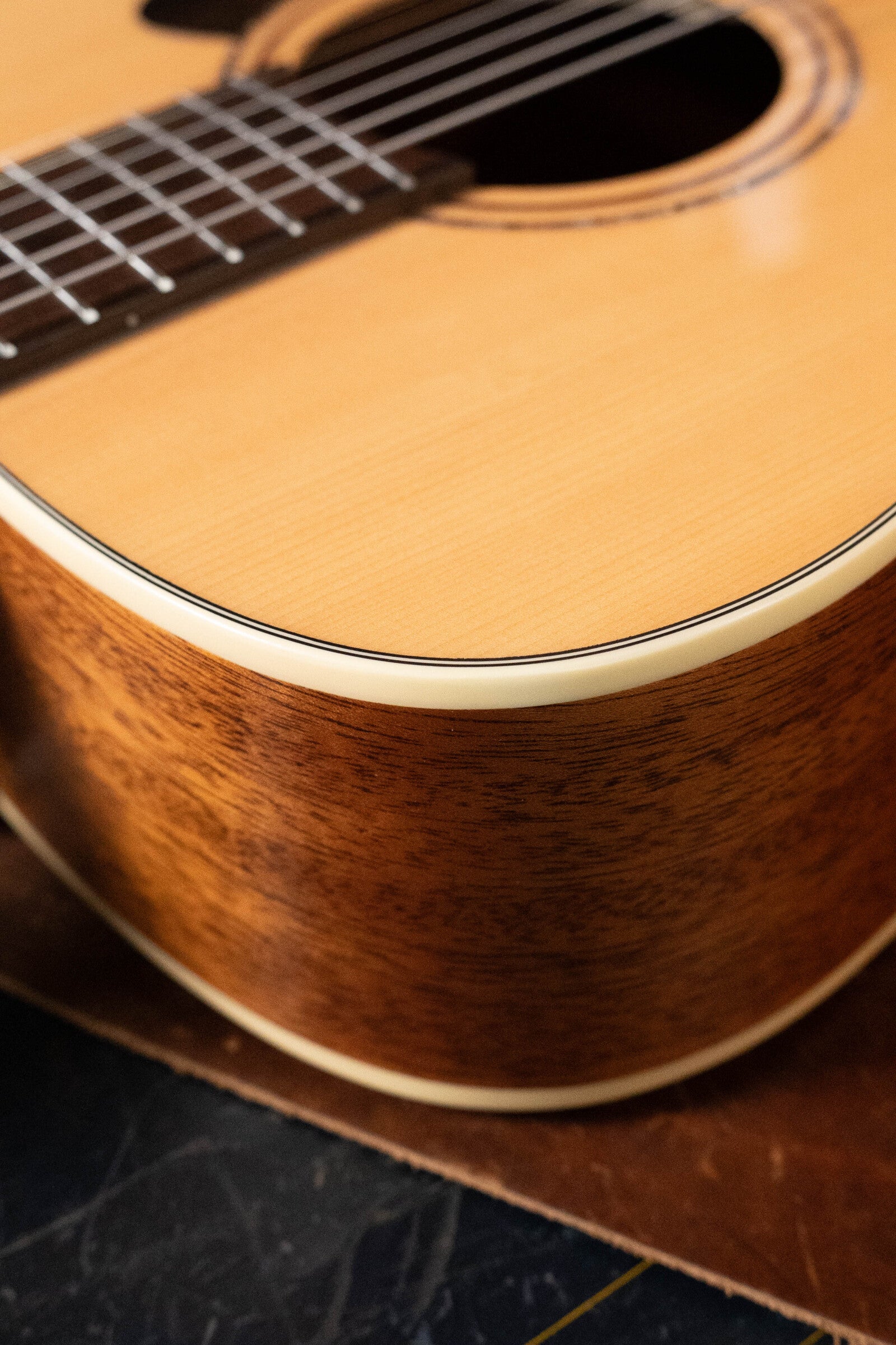 Close-up of a (Used) 2024 Alvarez AD60 Sitka/Mahogany Dreadnought Acoustic Guitar #0300, showcasing its smooth wooden body, cream binding, and fretboard as it rests on a dark surface.