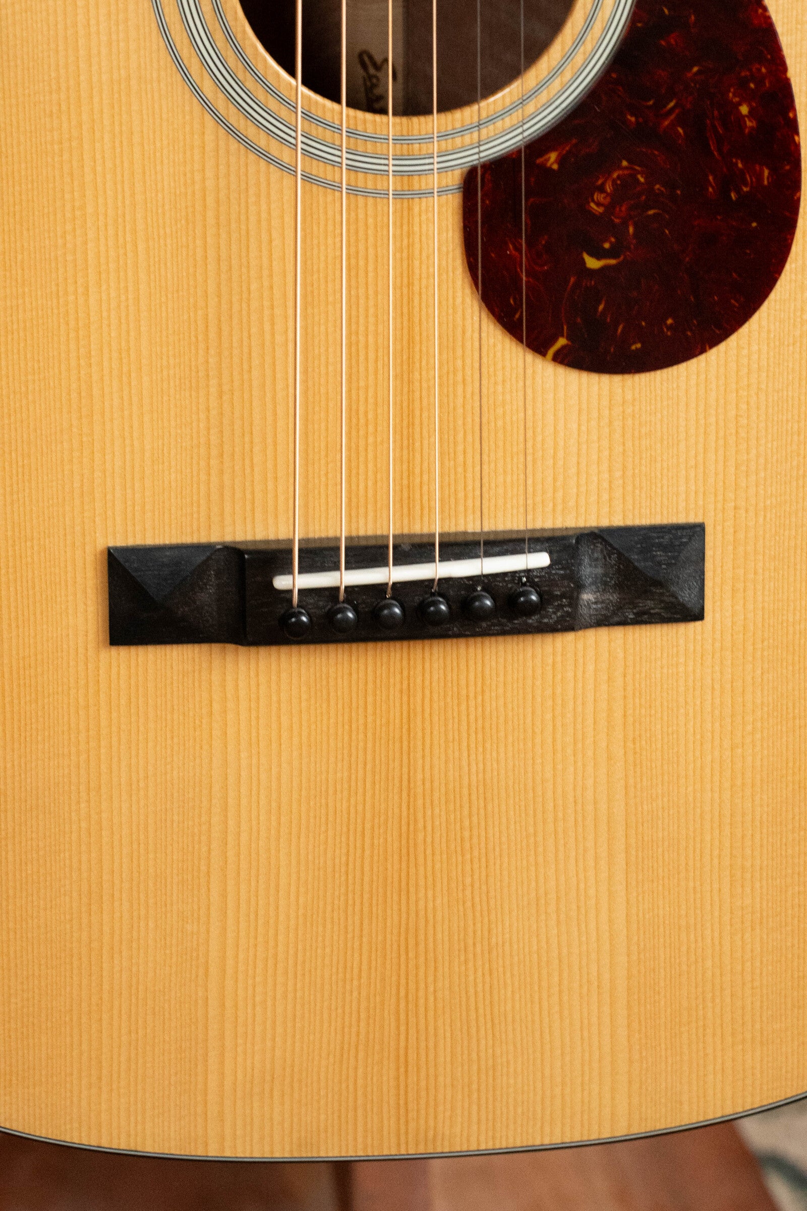 Close-up of a (Used) 2024 Eastman Guitars E10OO-TC Acoustic Guitar #0268, featuring a Thermo-Cure Adirondack Spruce top, strings, black bridge and pins, white saddle, tortoiseshell pickguard detail, and light wood finish.