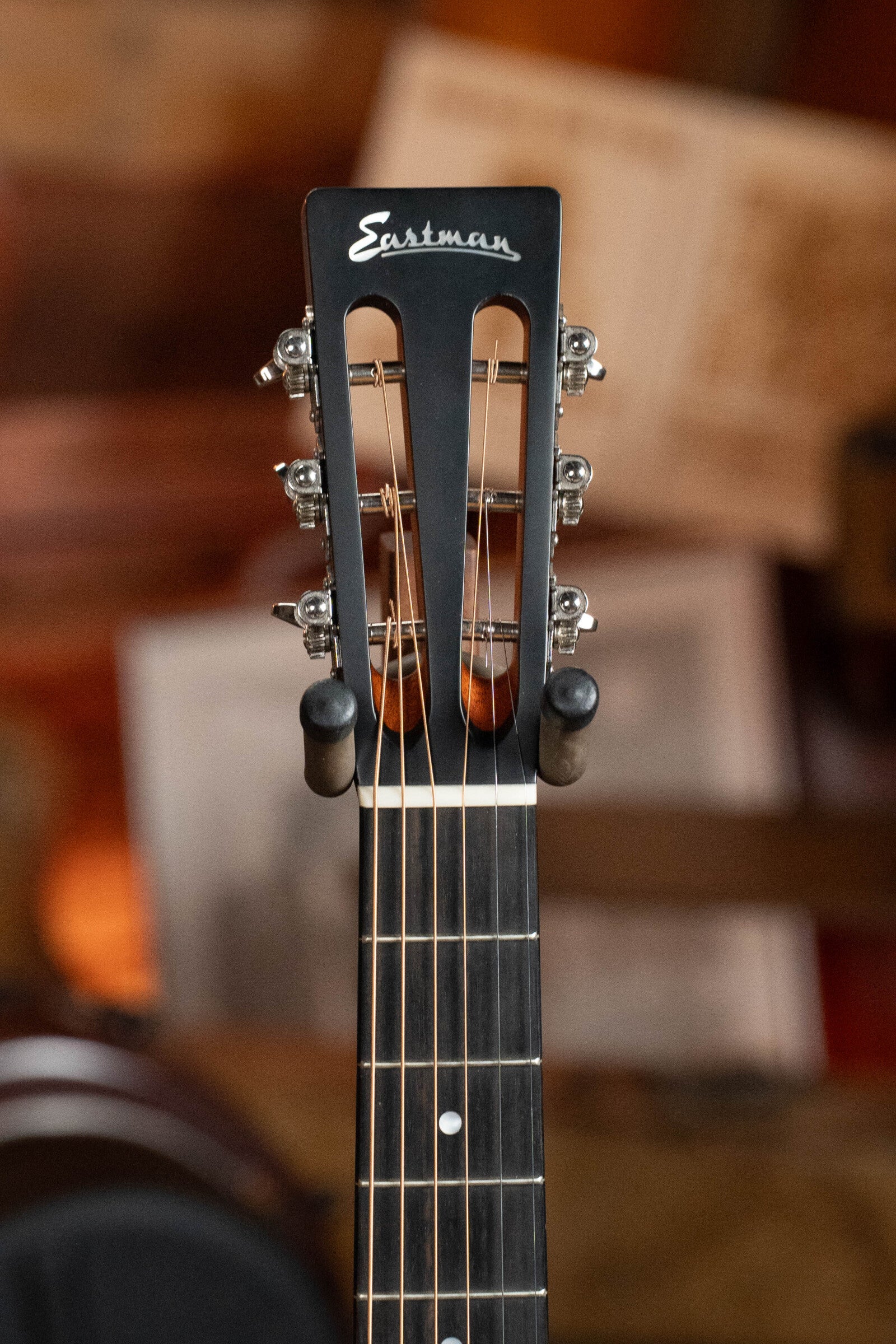 Close-up of the headstock of a (Used) 2024 Eastman Guitars E10OO-TC Thermo-Cure Adirondack/Mahogany Acoustic Guitar #0268, highlighting its slotted design, metal tuning pegs, and visible strings against a softly blurred background.