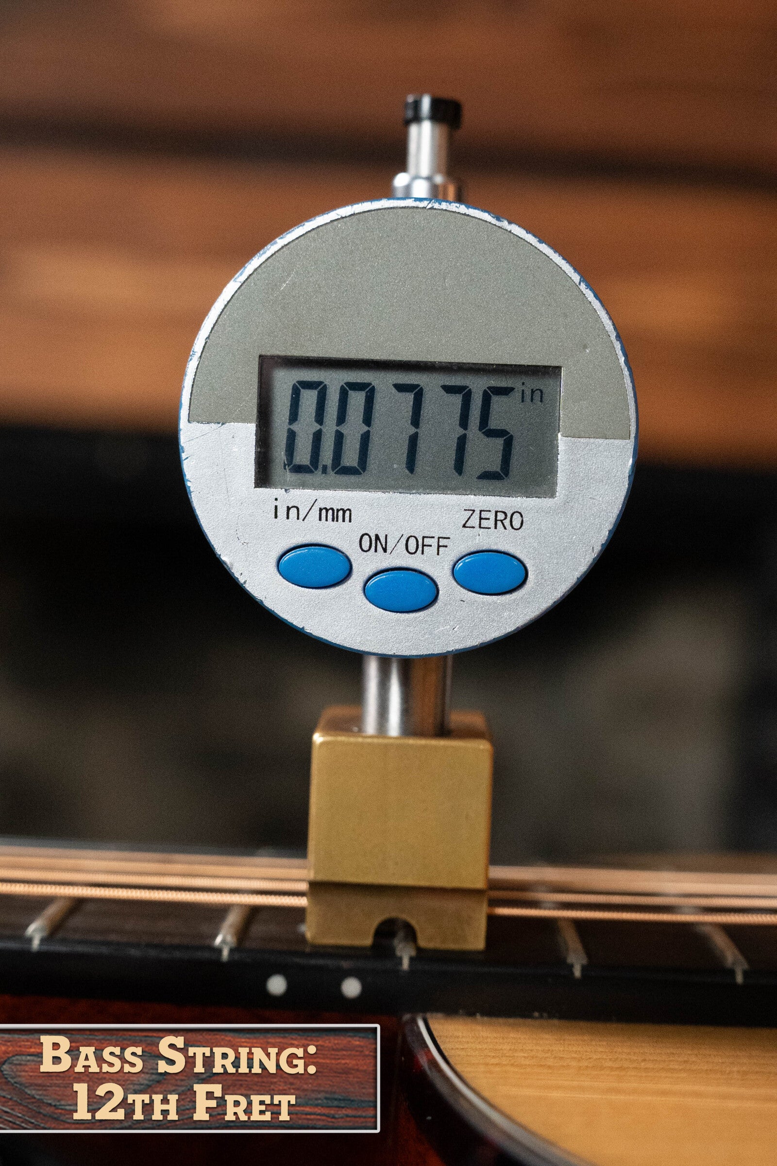 A digital gauge shows a bass guitar string height of 0.0775 inches at the 12th fret, with a label reading "Bass String: 12th Fret," similar to checks on an Eastman Guitars (Used) 2024 E10OO-TC Thermo-Cure Adirondack/Mahogany Acoustic Guitar #0268.