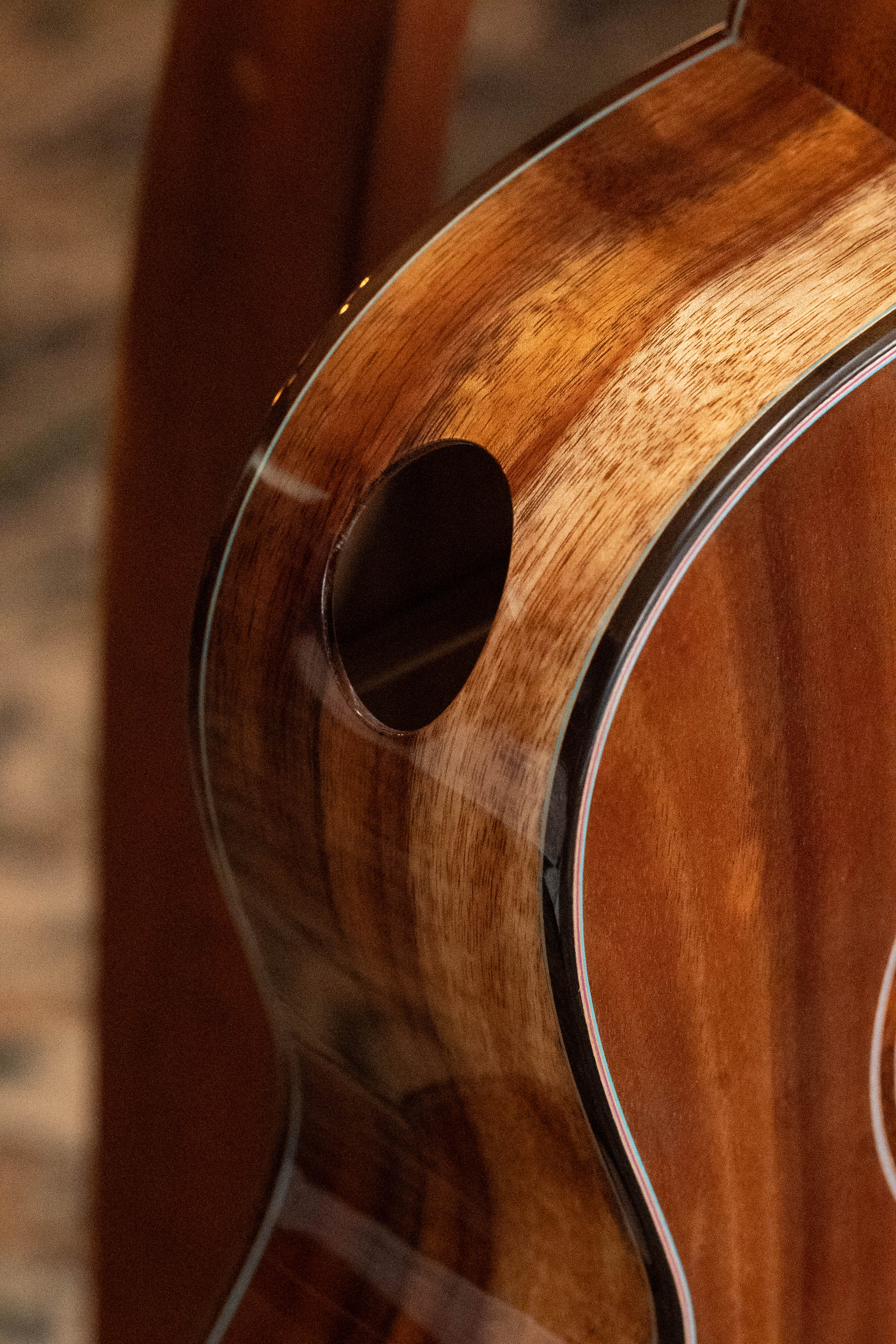 Close-up of a glossy (Used) 2025 Eastman L-OOSS-LTD-KOA Limited Edition All Koa Acoustic Guitar #9075 by Eastman Guitars, highlighting the wood grain, smooth finish, and side sound port with a softly blurred background.