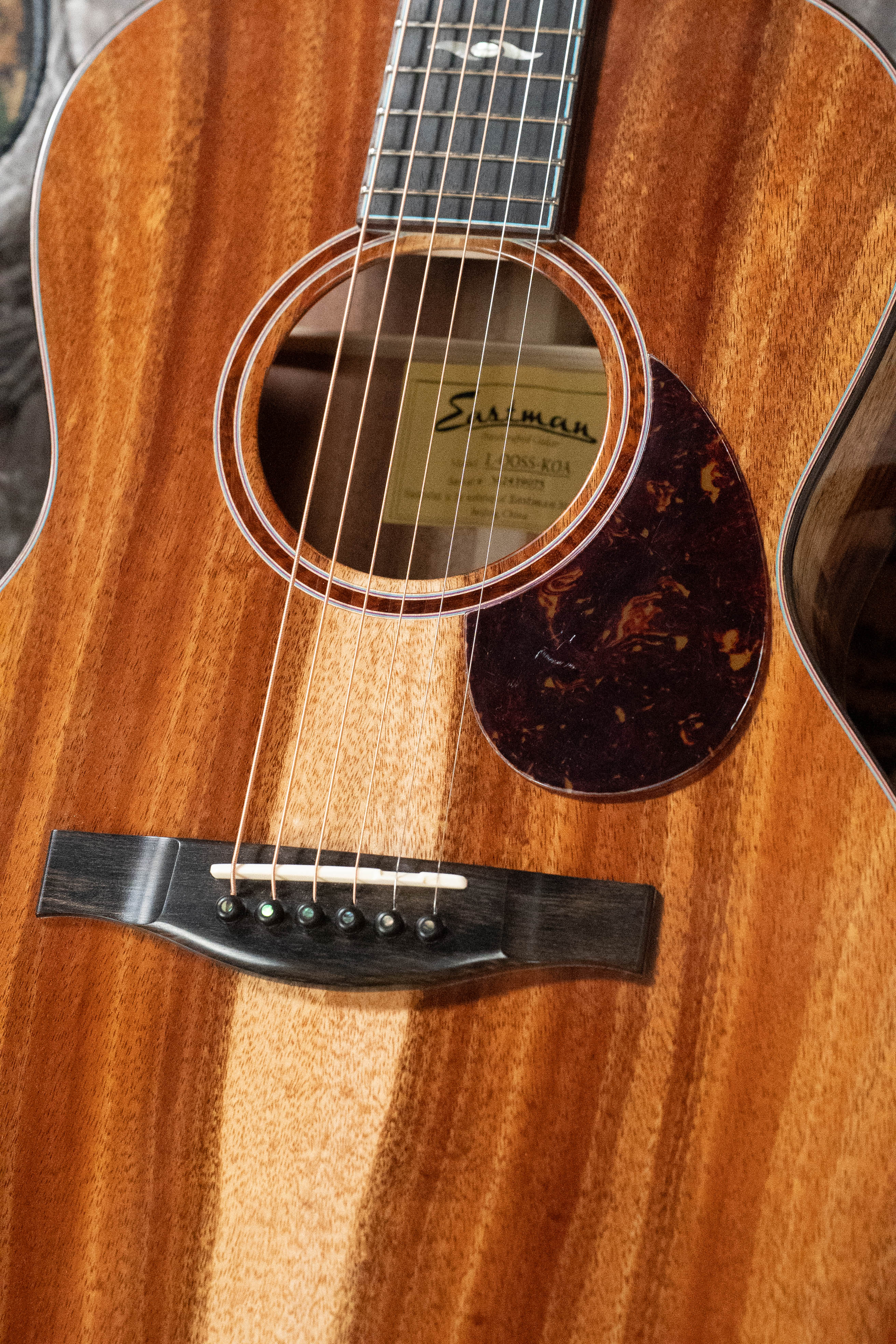 Close-up of a (Used) 2025 Eastman Guitars L-OOSS-LTD-KOA Limited Edition Luthier Series All Koa Acoustic Guitar #9075, showcasing its solid koa top, warm natural finish, rich wood grain, strings, tortoiseshell pickguard, and soundhole label.