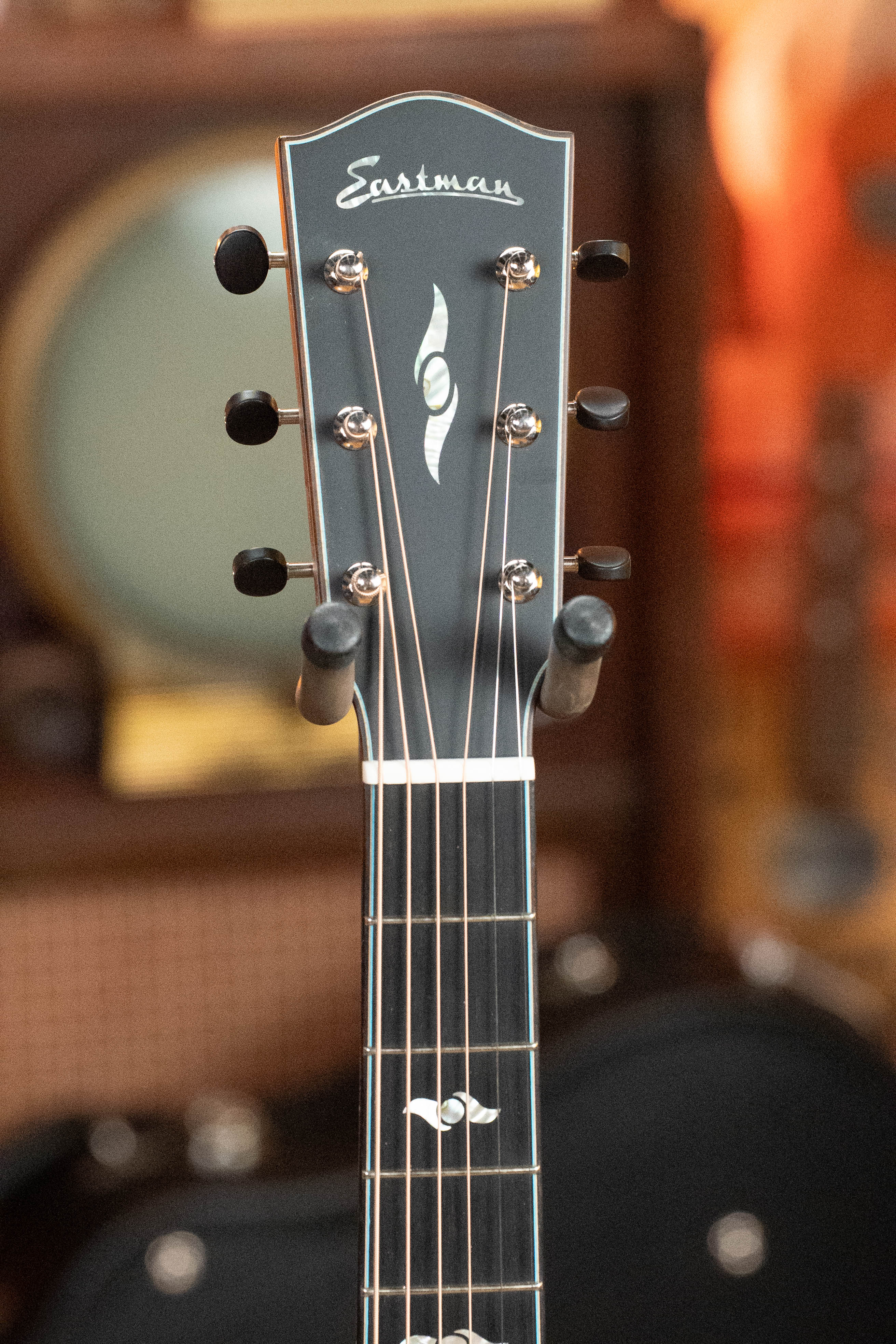 Close-up of the headstock on a (Used) 2025 Eastman L-OOSS-LTD-KOA Limited Edition Luthier Series All Koa Acoustic Guitar #9075 by Eastman Guitars, highlighting tuning pegs, the logo, and inlays with a blurred background.