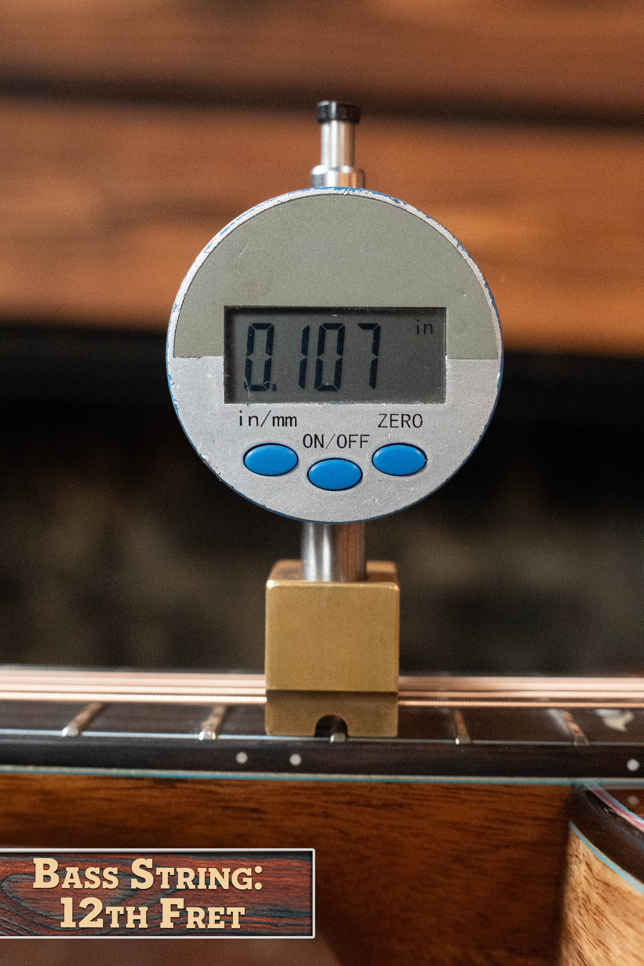 A digital gauge shows 0.107 inches for the string height at the 12th fret of a (Used) 2025 Eastman L-OOSS-LTD-KOA Limited Edition Luthier Series All Koa Acoustic Guitar #9075 by Eastman Guitars. A sign reads “Bass String: 12th Fret.”.