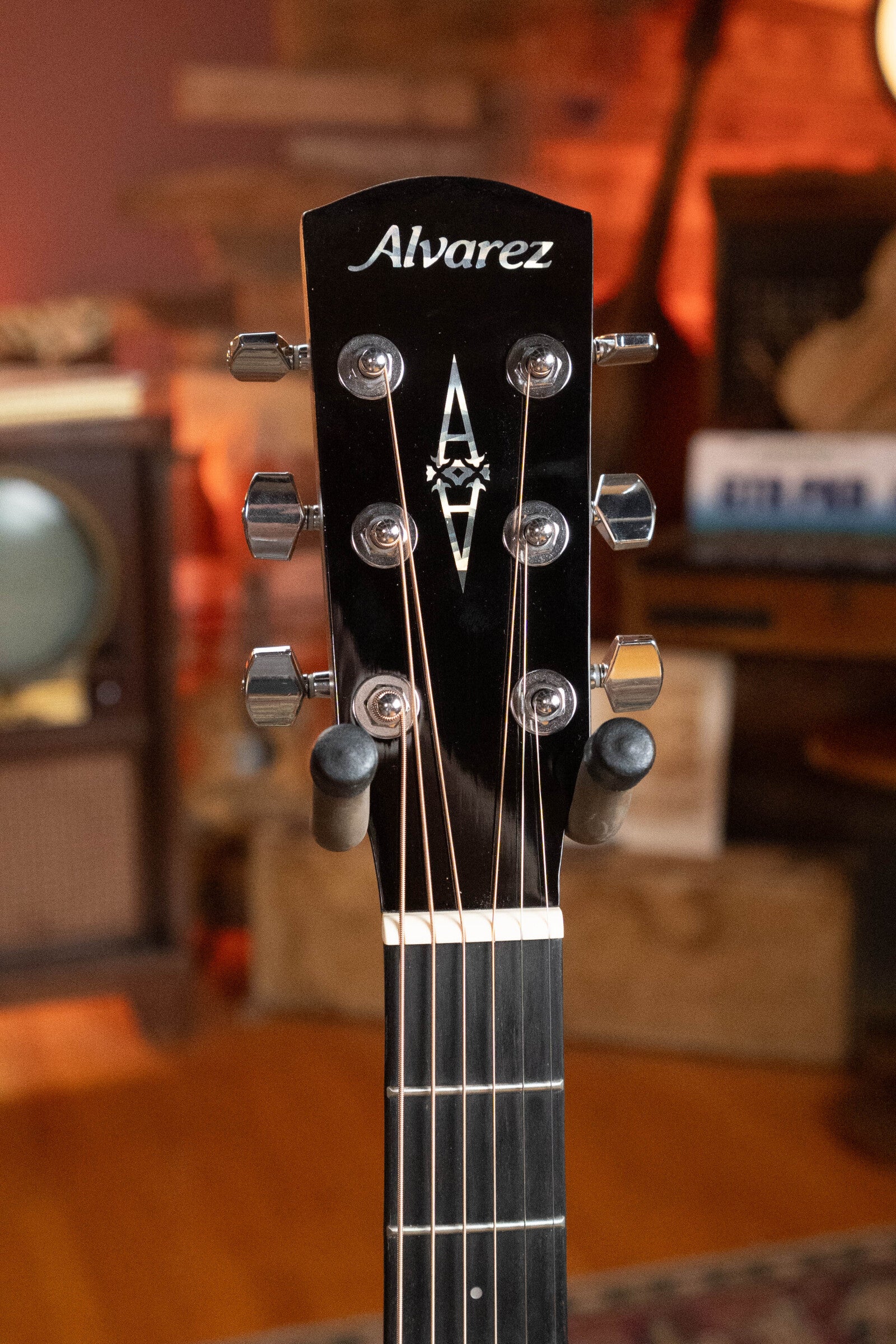 Close-up of the headstock on a (Used) 2025 Alvarez RD-26 Spruce/Mahogany Dreadnought Acoustic Guitar #0161, highlighting tuning pegs, strings, and the Alvarez logo. A retro TV and cozy room decor appear in the background.