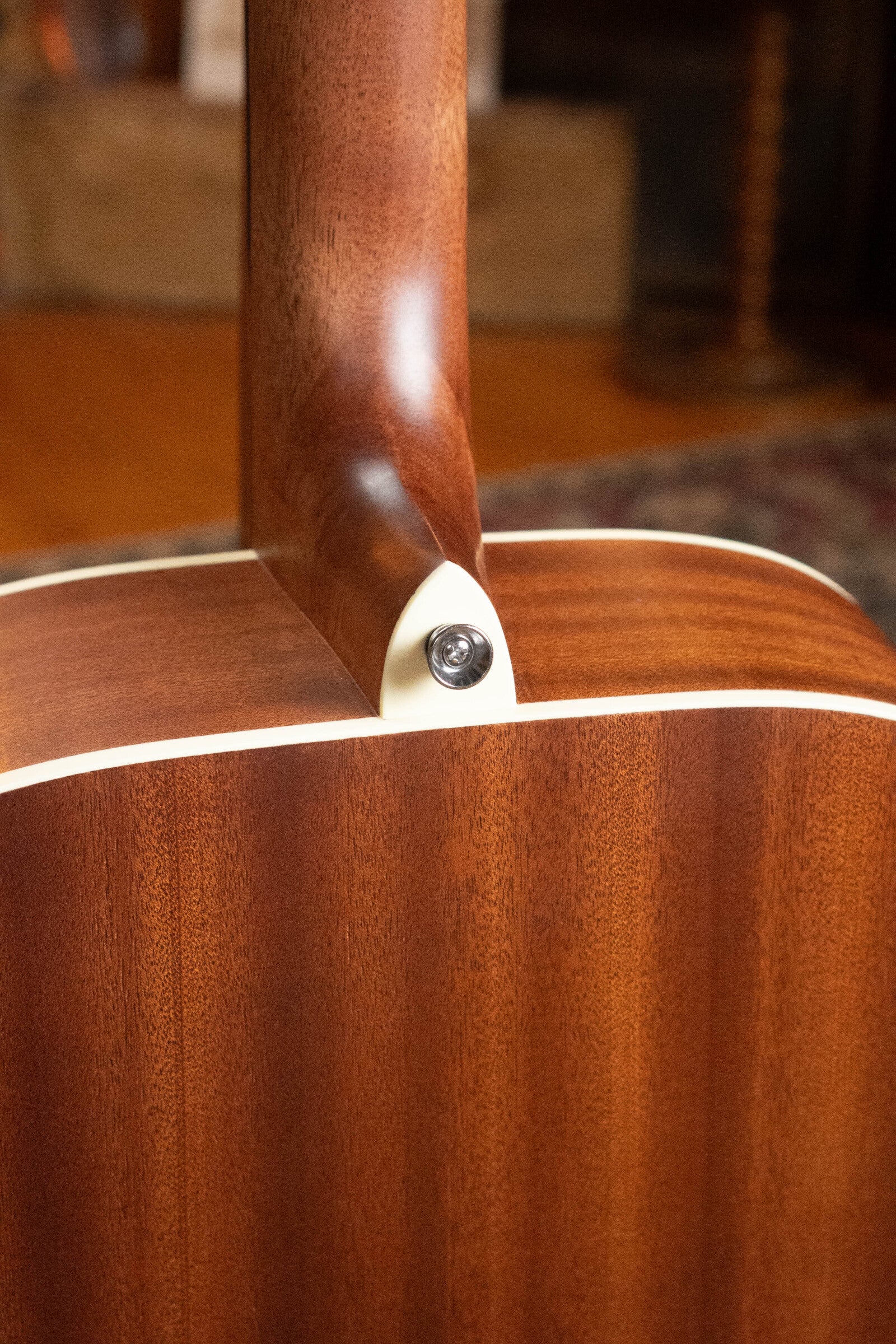 Close-up of the neck joint and metal strap button on the heel of a (Used) 2025 Alvarez RD-26 Spruce/Mahogany Dreadnought Acoustic Guitar #0161, with a blurred background. Ideal for highlighting details of this student-friendly Alvarez guitar.
