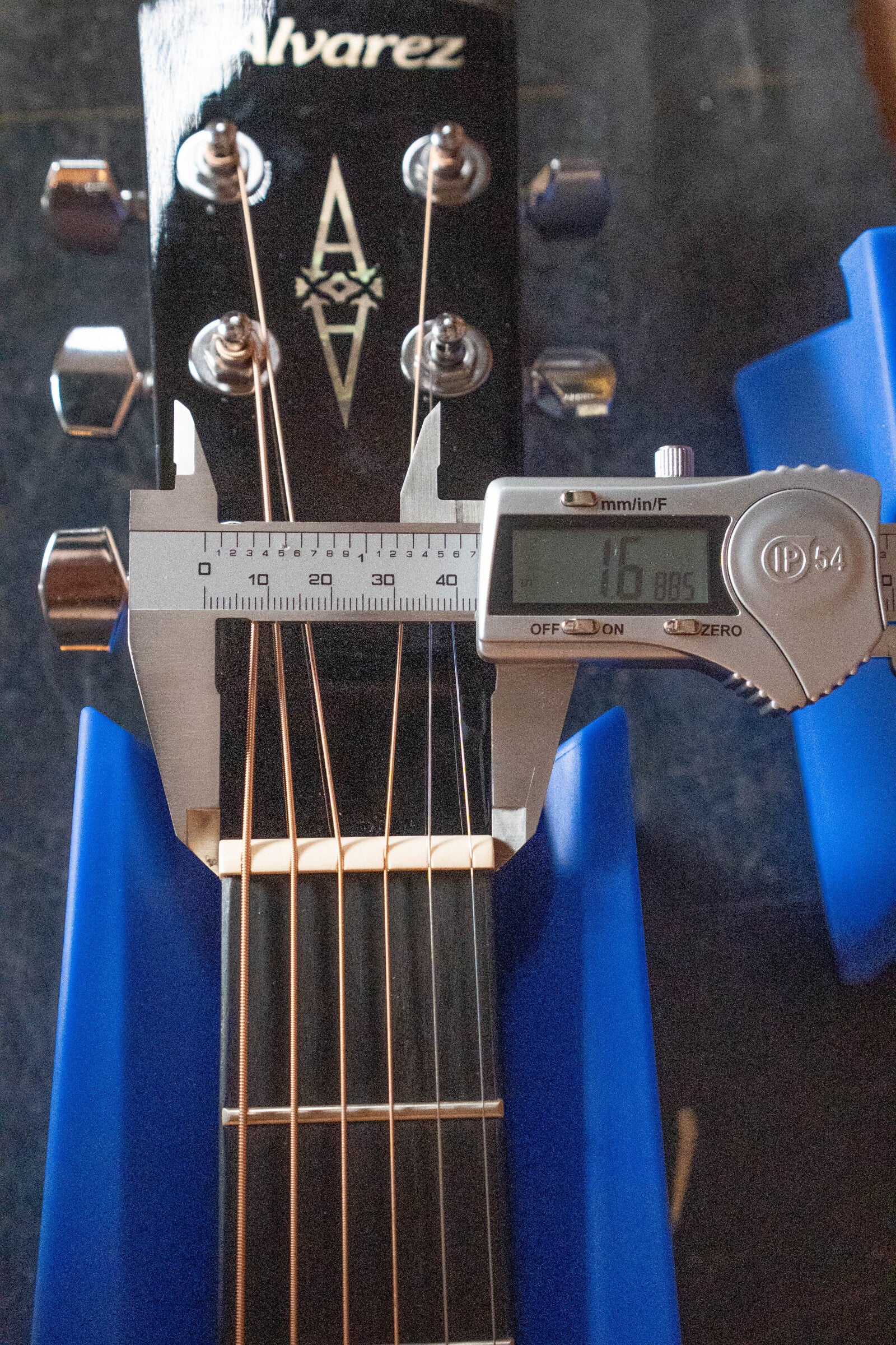 A digital caliper measures the nut width of a (Used) 2025 Alvarez RD-26 Spruce/Mahogany Dreadnought Acoustic Guitar #0161, displaying 1.686 inches; the student-friendly guitar is stabilized with blue supports.