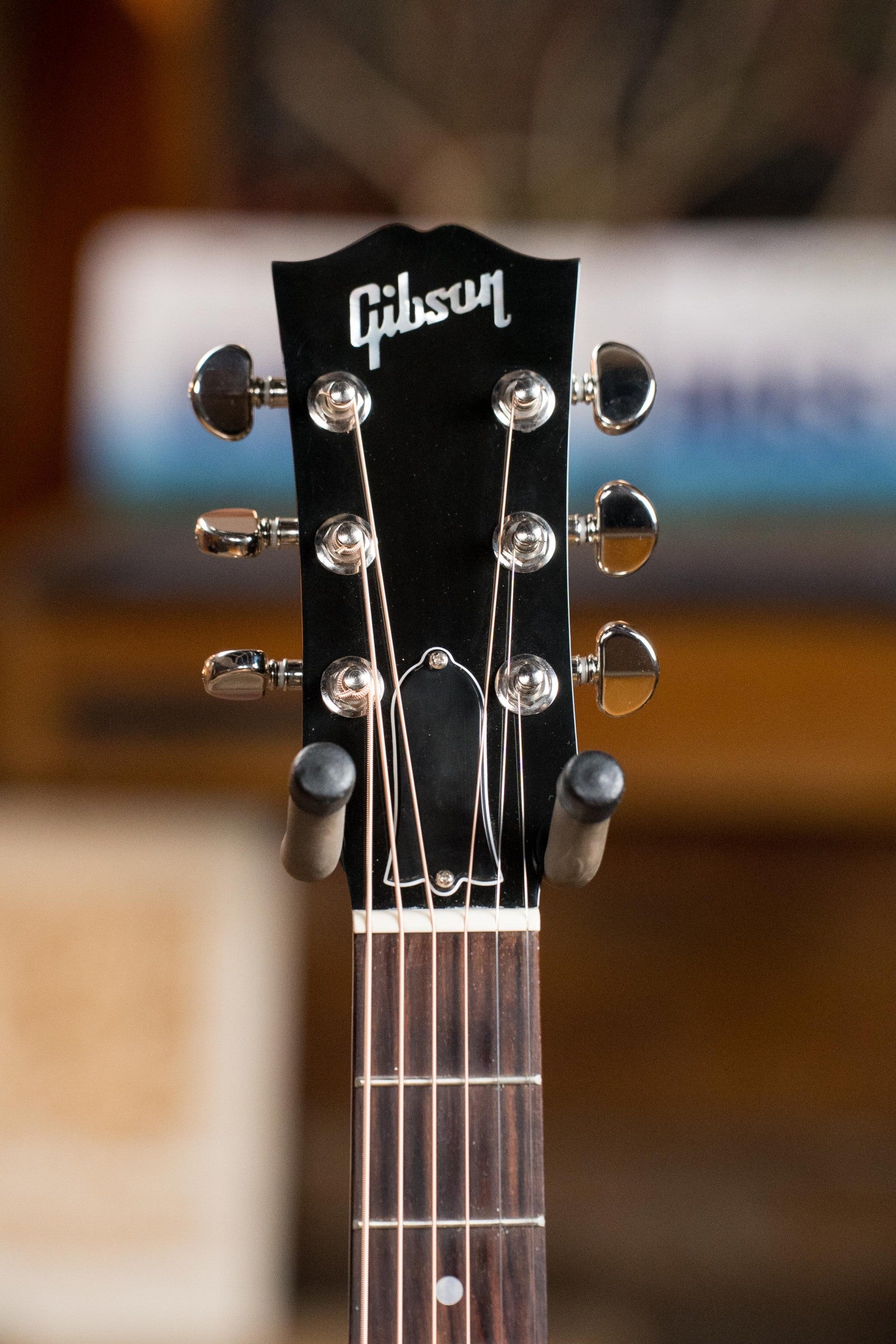 Close-up of the headstock on a used Gibson J45 Standard Sitka/Mahogany Round Shoulder Vintage Sunburst Dreadnought Guitar w/K&K Pickup #4111, showing tuning pegs and fretboard with Gibson logo; softly blurred background.