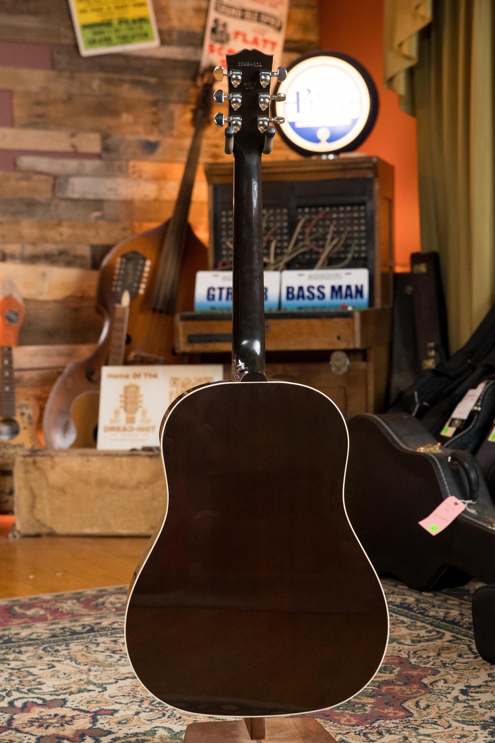 A used Gibson J45 Standard Sitka/Mahogany Vintage Sunburst Dreadnought Guitar w/K&K Pickup (#4111) stands upright in a cozy room filled with musical instruments, vintage decor, and an orange wall in the background.