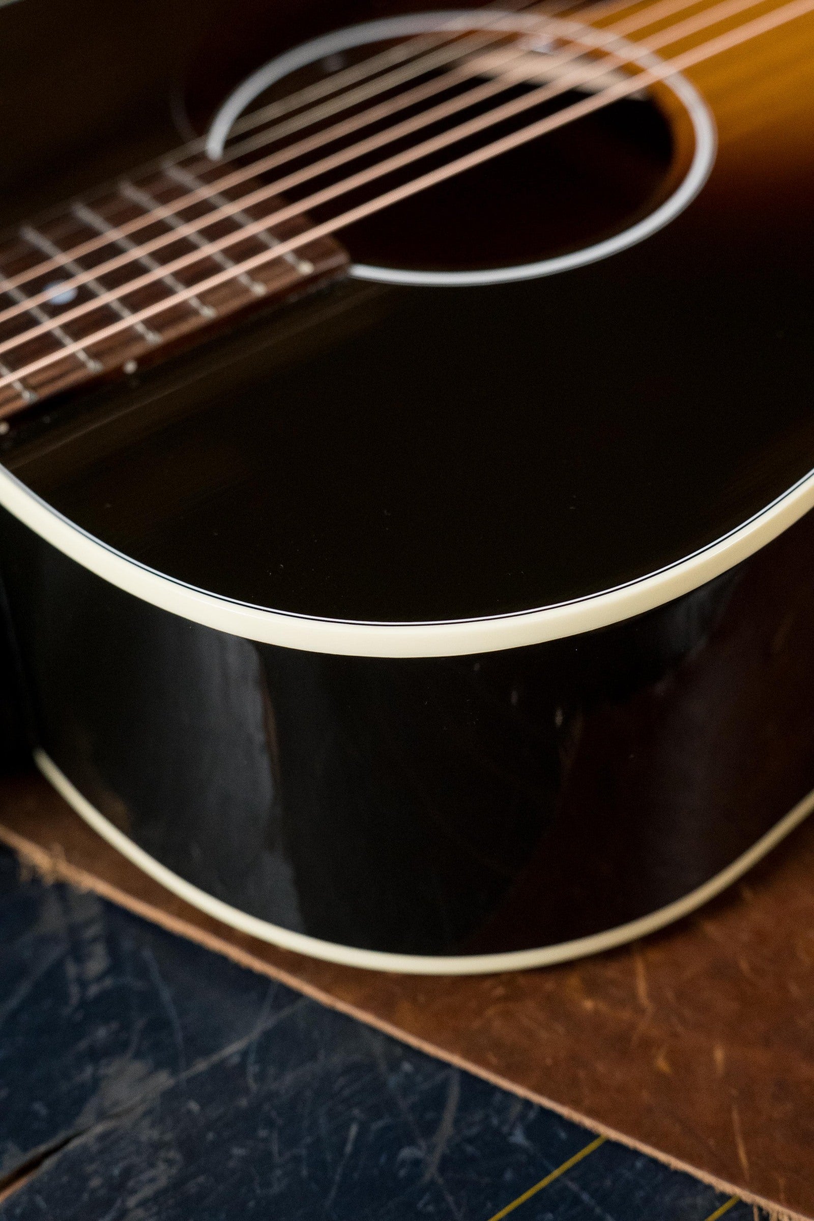 Close-up of a used Gibson J45 Standard Sitka/Mahogany Round Shoulder Vintage Sunburst Dreadnought guitar with K&K Pickup (#4111), showing its glossy finish and part of the fretboard, resting on a wooden surface.