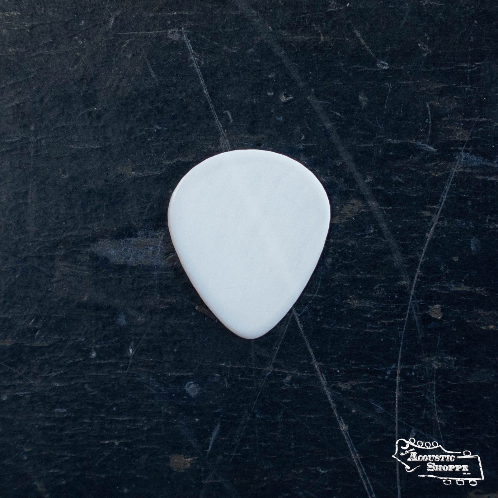 A Wegen Picks NH140 Bluegrass Acoustic Guitar Pick, White, 1.4mm (pack of 4), rests on a dark textured surface—perfect for fans of boutique guitars and premium acoustic accessories.