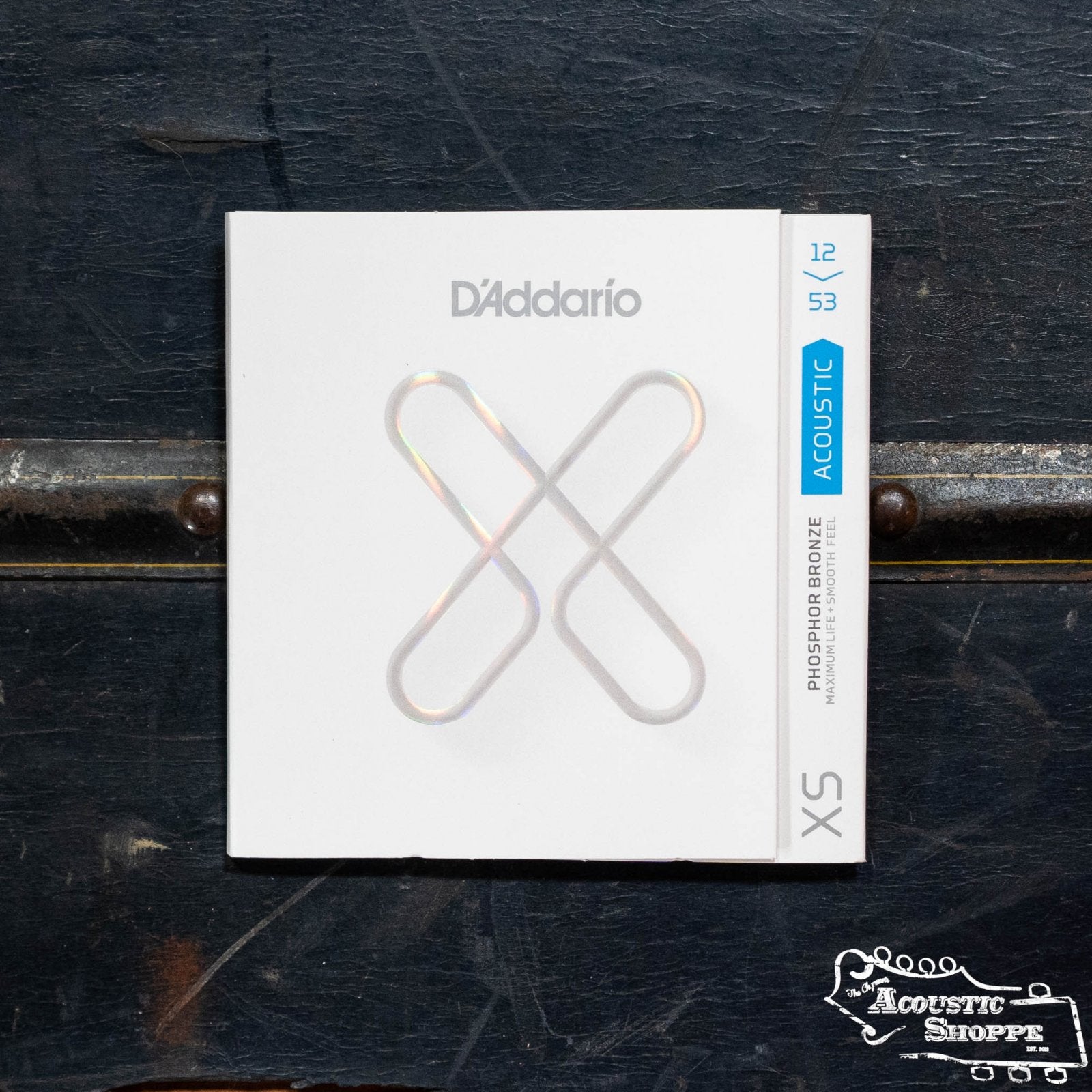 A DAddario XSAPB1253 XS Acoustic Phosphor Bronze Light 12-53 guitar string pack is displayed on a dark textured surface with The Acoustic Shoppe logo in the bottom right corner.