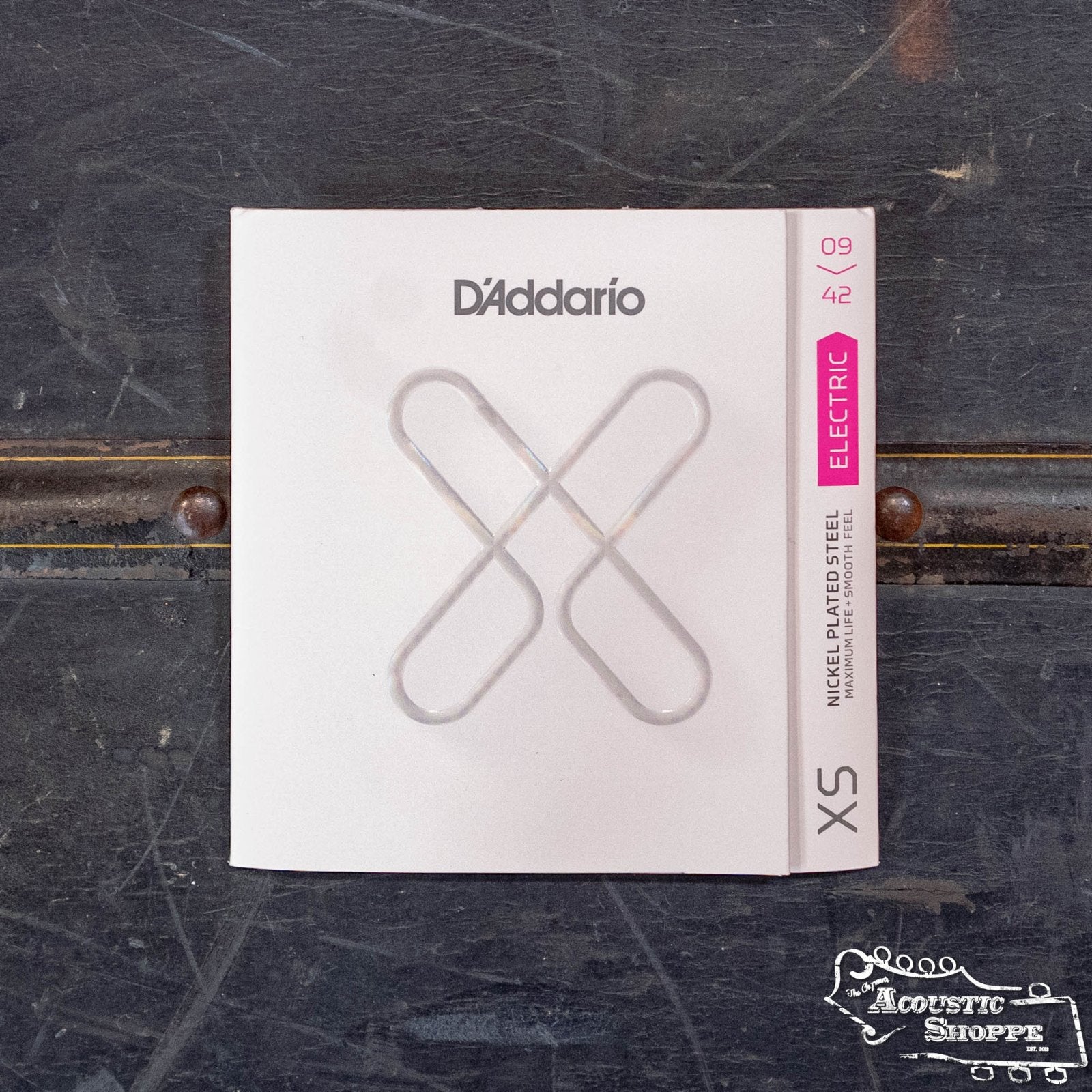 A pack of DAddario XSE0942 XS Super Light Nickel Coated Electric Guitar Strings (09-42) sits on a dark surface, featuring white packaging with a large silver X and Acoustic Shoppe branding in the lower right corner.