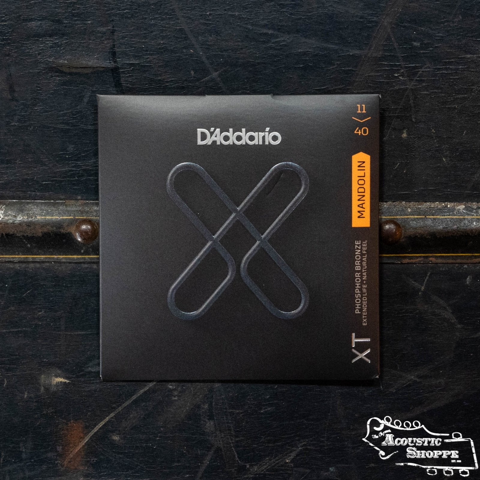 A box of DAddario XTM1140 Phosphor Bronze Medium Mandolin Strings (11-40 gauge) sits on a dark, textured surface, featuring The Acoustic Shoppe logo in the bottom right corner as your trusted acoustic instrument dealer.
