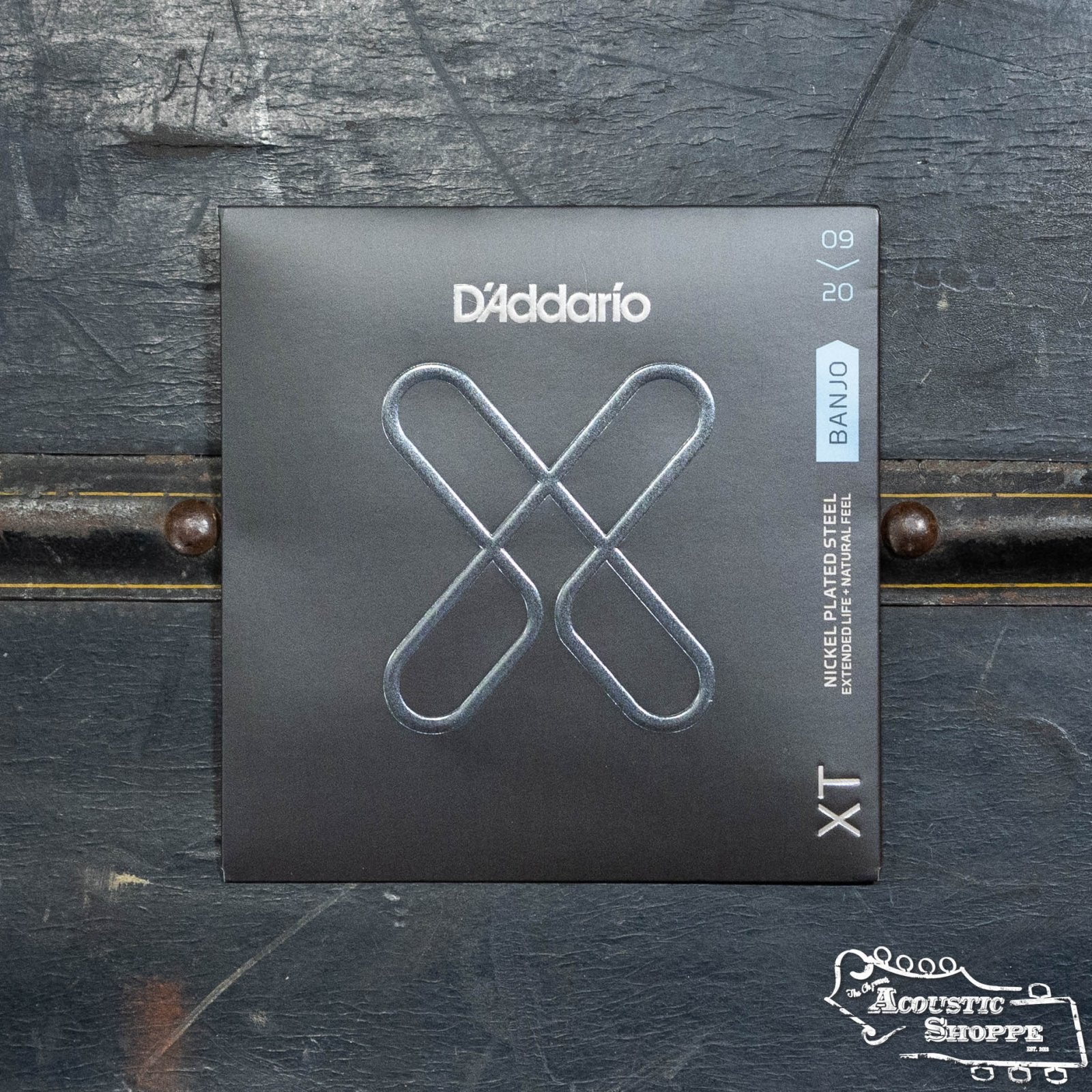 A pack of DAddario XTJ0920 XT Banjo Nickel Plated Steel Light 09-20 strings, known for their polymer coating and durability, sits on a dark wooden surface with The Acoustic Shoppe logo in the bottom right corner.