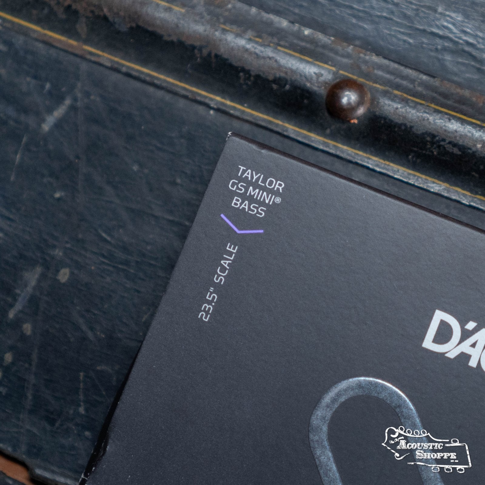 Close-up of a box corner labeled D'Addario XTB3790GS Phosphor Bronze Custom Light Taylor GS Mini Coated Acoustic Bass String Set 37-90, with a metallic rivet in the background. The Acoustic Shoppe logo is visible, highlighting this premium D'Addario set.