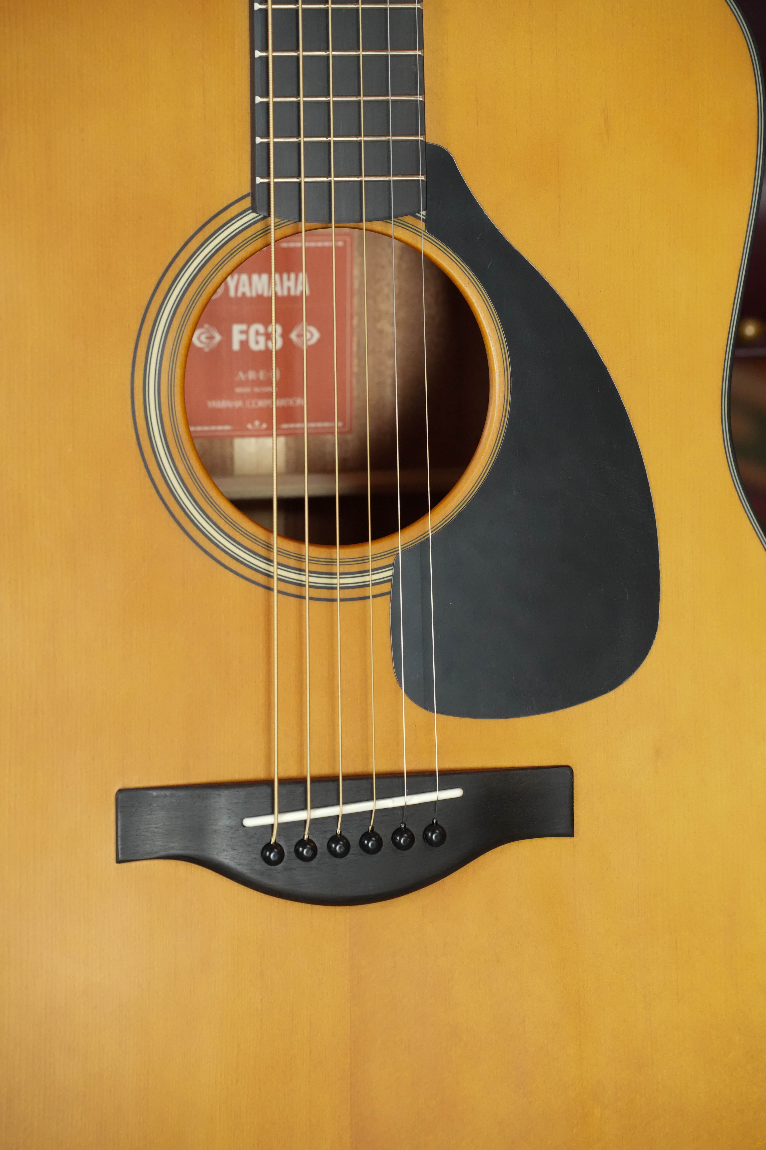 Close-up of the Yamaha FG3 Red Label Dreadnought Acoustic Guitar #1210 body, showing six strings, a black pickguard, part of the soundhole, and the FG-8 label inside.