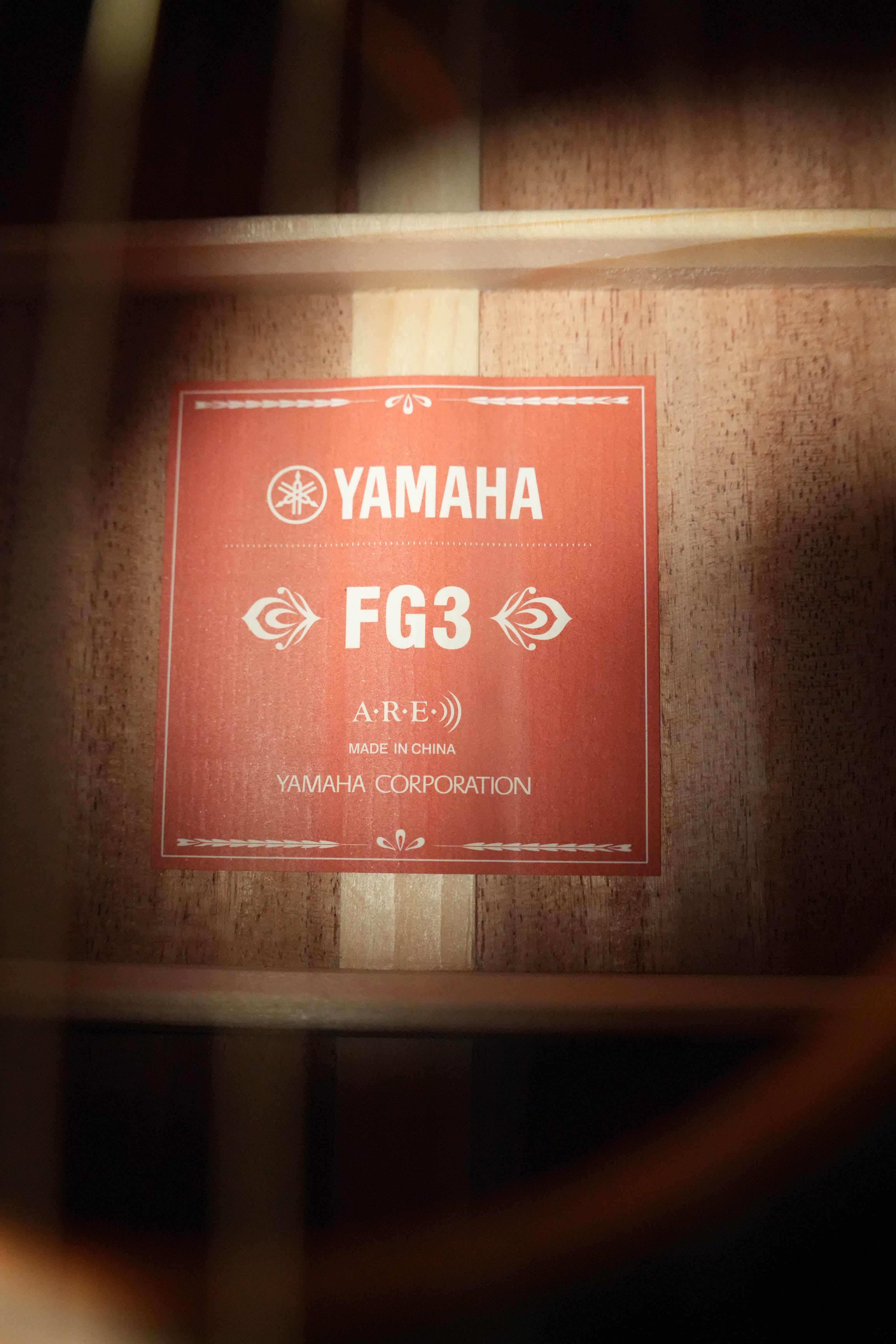 Close-up of a Yamaha FG3 Red Label Dreadnought Acoustic Guitar #1210, showing the red label with Acoustic Resonance Enhancement (A.R.E.) inside, wooden braces, and part of the body visible.