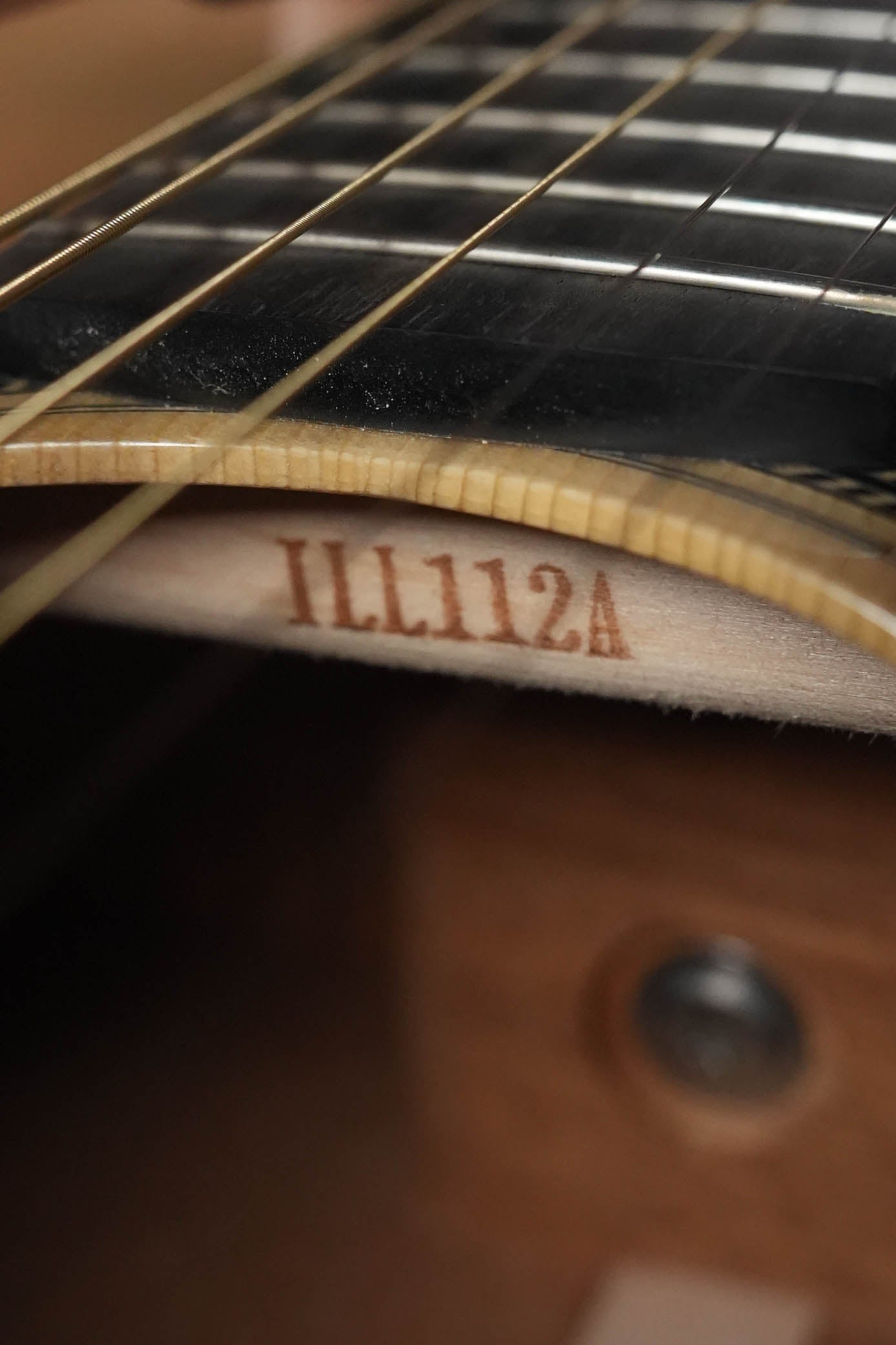 Close-up of the Yamaha FG9 M Adirondack/Mahogany Dreadnought Acoustic Guitar #112A neck, focusing on the area under the strings where "112A" is stamped near the body. Metal frets and strings showcase its resonant acoustic tone and Adirondack spruce top.