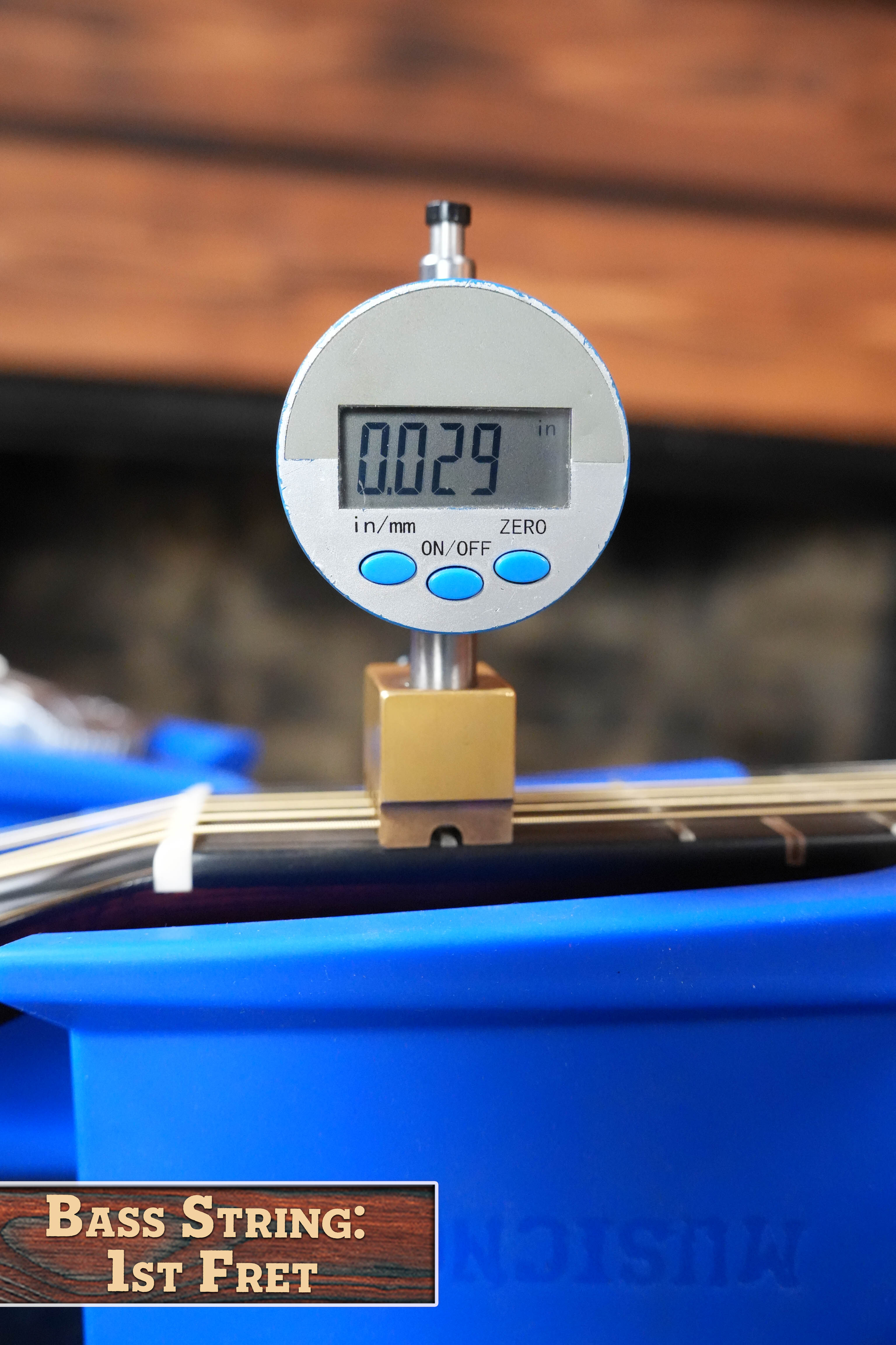 A digital gauge shows 0.029" while measuring bass string height at the 1st fret on a Yamaha FG9 M Adirondack/Mahogany Dreadnought Acoustic Guitar #112A. Blue container below; text: BASS STRING: 1ST FRET. Brand: Yamaha.