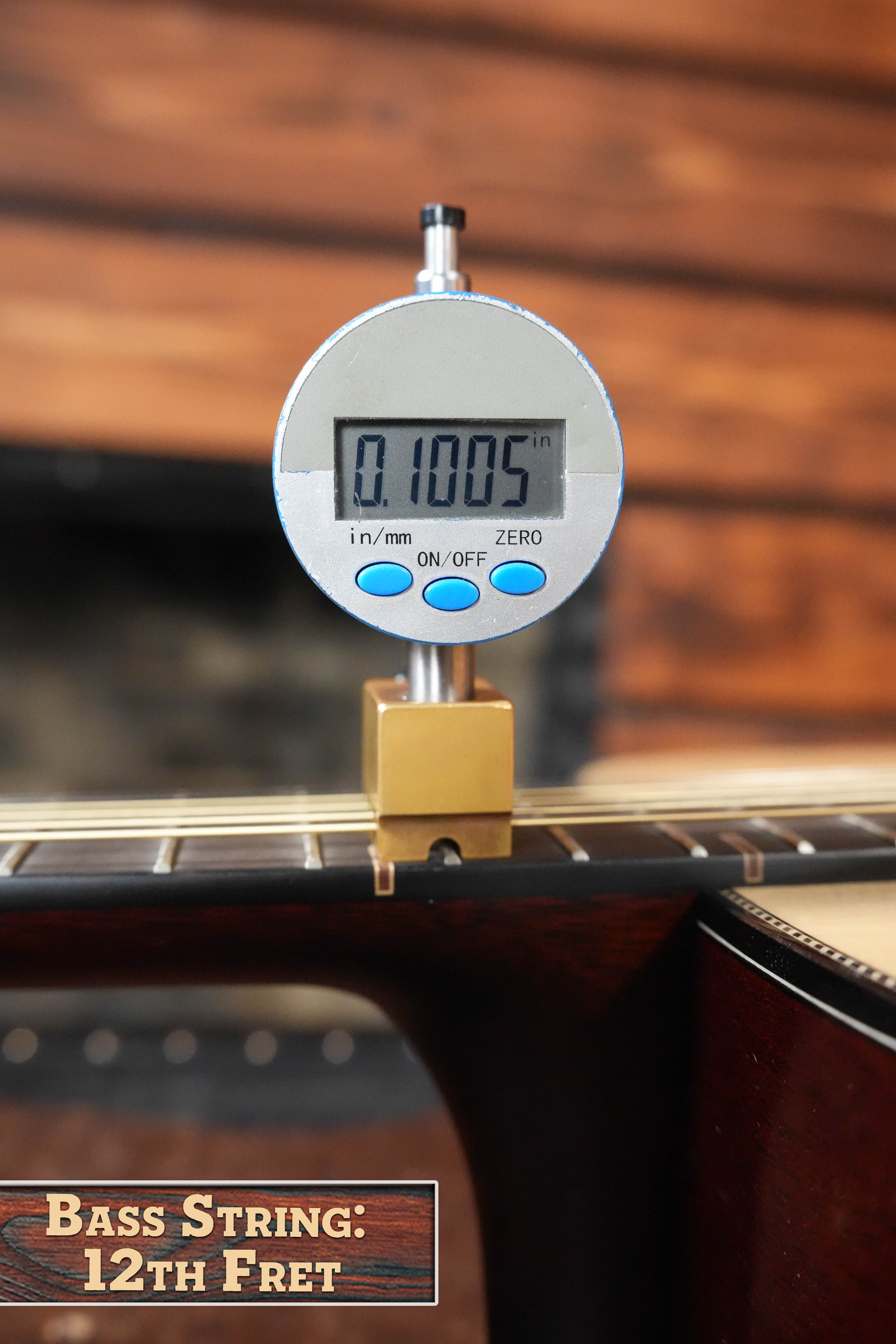 A digital gauge measures the string height above the 12th fret of a Yamaha FG9 M Adirondack/Mahogany Dreadnought Acoustic Guitar #112A, displaying 0.1005 in. The wooden background and label highlight this Yamaha acoustic instrument.