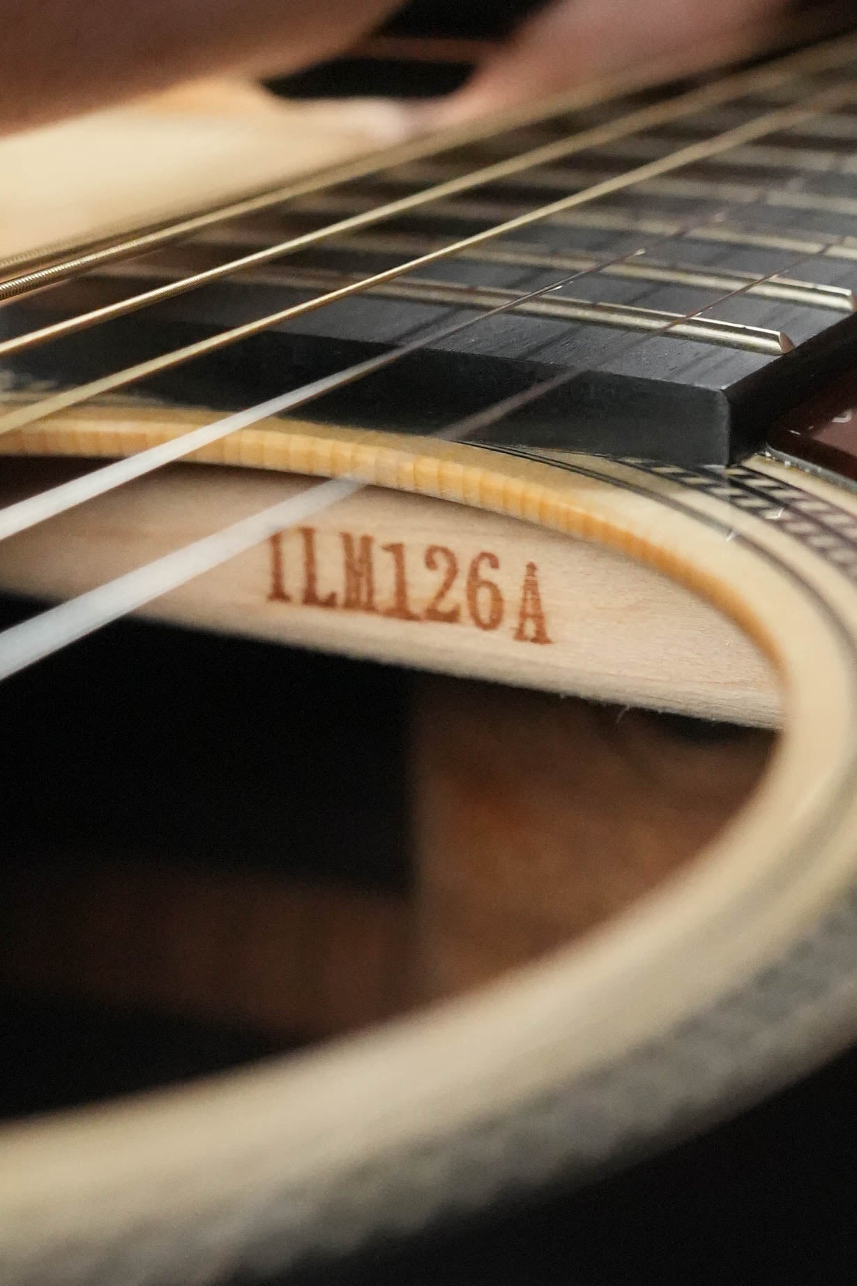 Close-up of a Yamaha FG9 R NT Natural Finish Dreadnought Acoustic Guitar’s sound hole, showing strings, part of the fretboard, and label #126A inside.