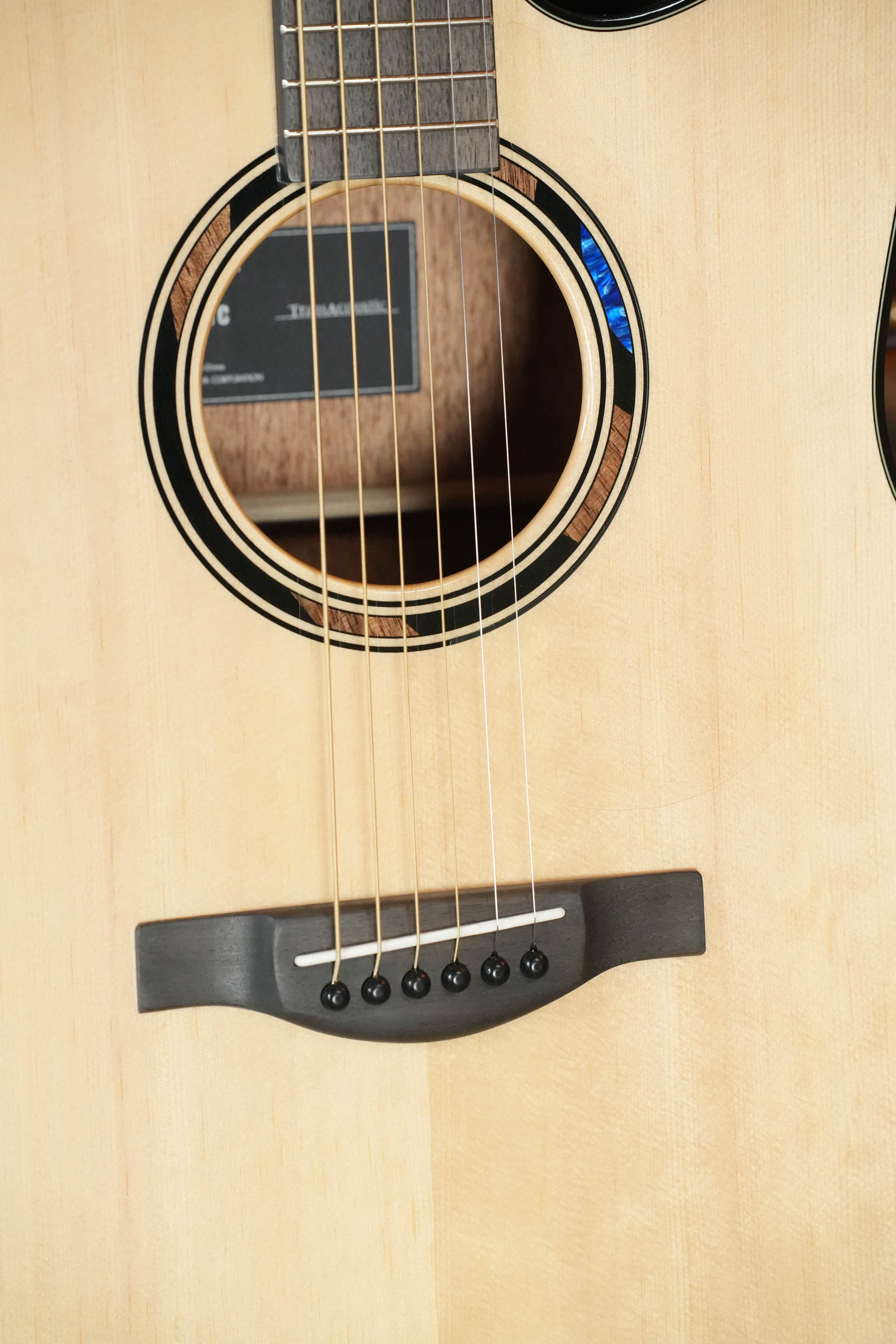 Close-up of the Yamaha TAG1 C Natural Finish Dreadnought Cutaway Acoustic-Electric Guitar, showing its sound hole, strings, and bridge on a light wood body with built-in effects for enhanced sound.