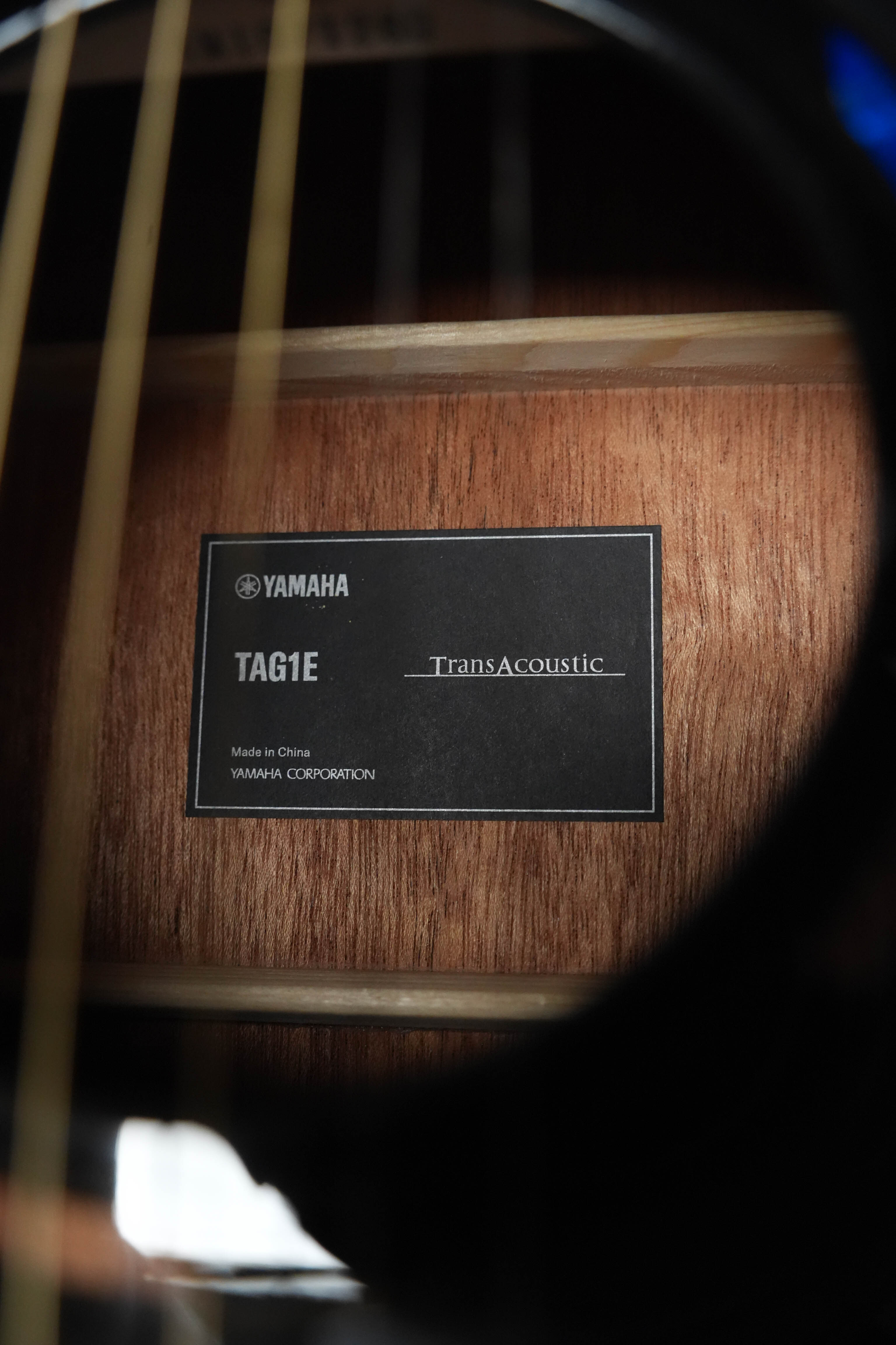 Close-up view through the sound hole of a Yamaha TAG1E TBL Spruce/Mahogany TransAcoustic Dreadnought Guitar, revealing an internal label with the model name, attached to the solid spruce and mahogany interior.