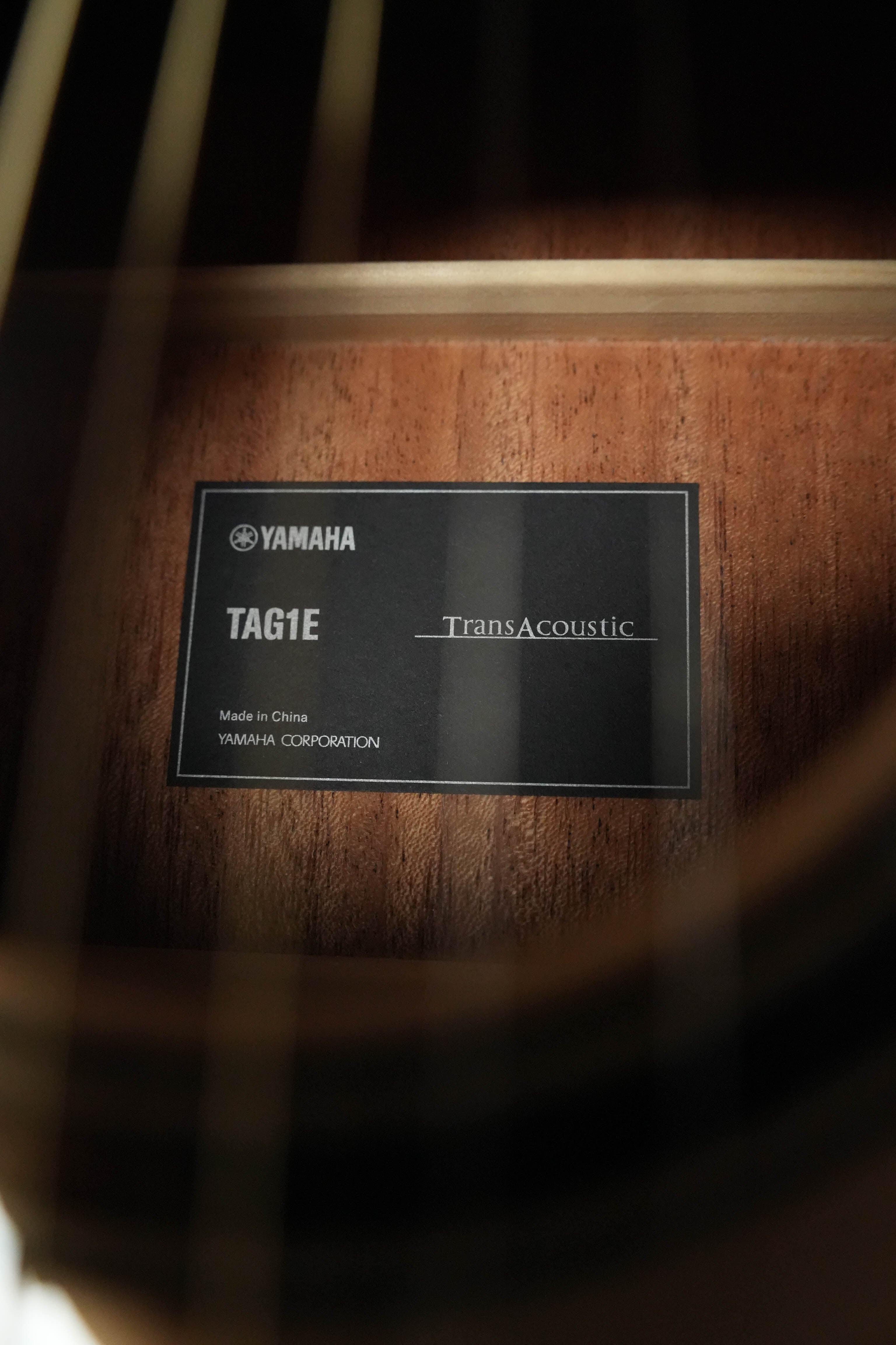 Close-up of a Yamaha TAG1E TransAcoustic Natural Finish Dreadnought Acoustic-Electric Guitar #1116 label inside the body, with visible guitar strings and wooden interior in the foreground.