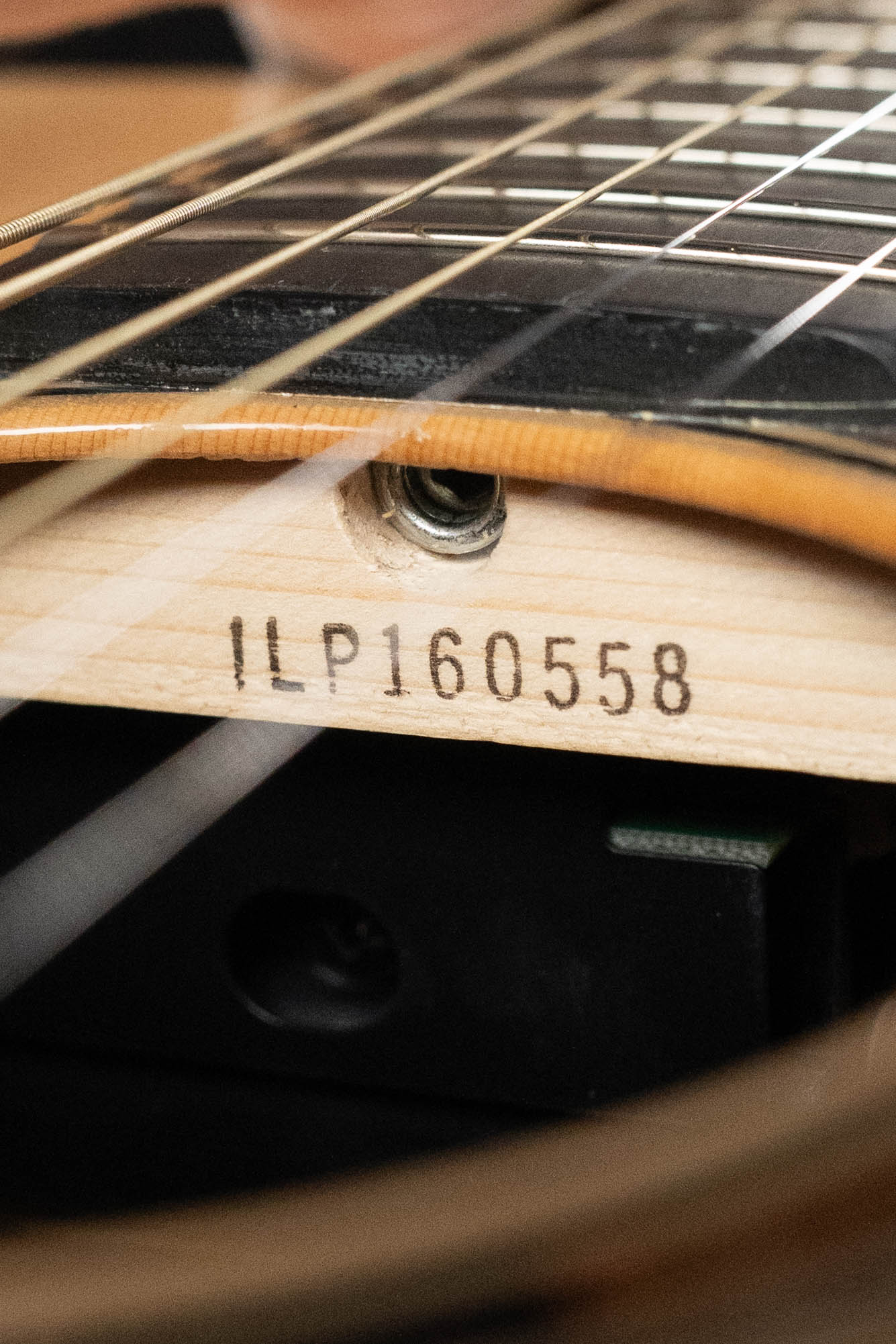 Close-up of serial number 0558 stamped inside a Yamaha TAG3C-NT Sitka/Mahogany Natural Dreadnought Guitar with the newest TransAcoustic System, showing part of the strings and fretboard above.