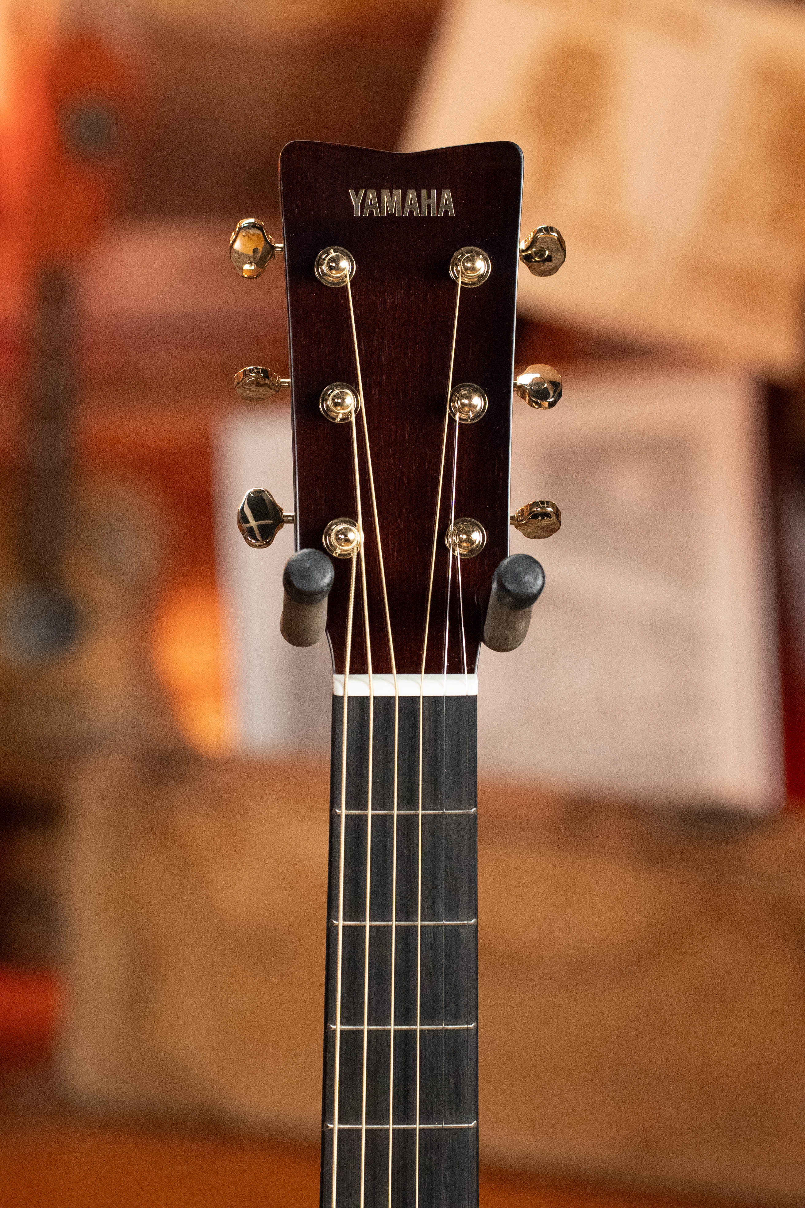 Close-up of the Yamaha TAG3C-NT Sitka/Mahogany Natural Dreadnought headstock shows tuning pegs and strings, with a warm, blurred background. Enjoy built-in effects from the latest TransAcoustic System in this stunning Yamaha guitar.