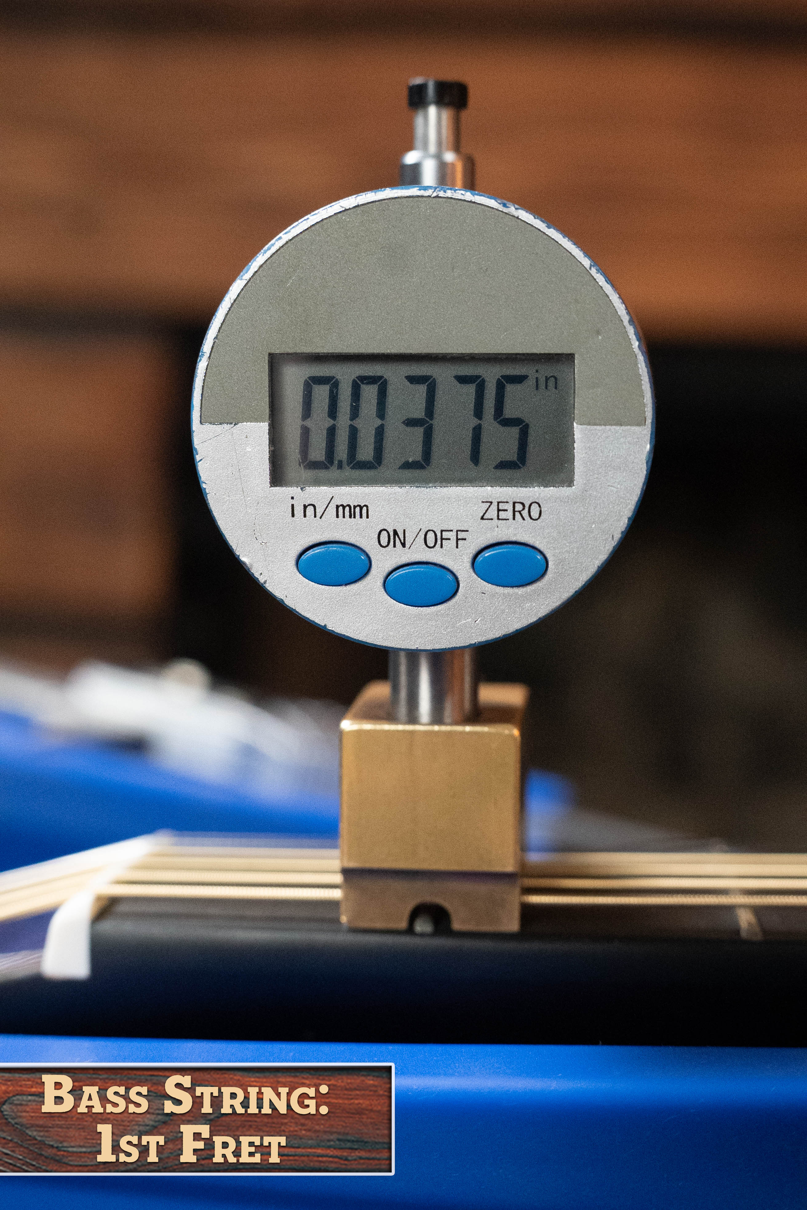 A digital gauge shows the Yamaha TAG3C-NT Sitka/Mahogany Dreadnought Guitar’s bass string height at 0.0375 inches above the 1st fret, with “Bass String: 1st Fret” displayed on a wooden sign in the lower left corner.